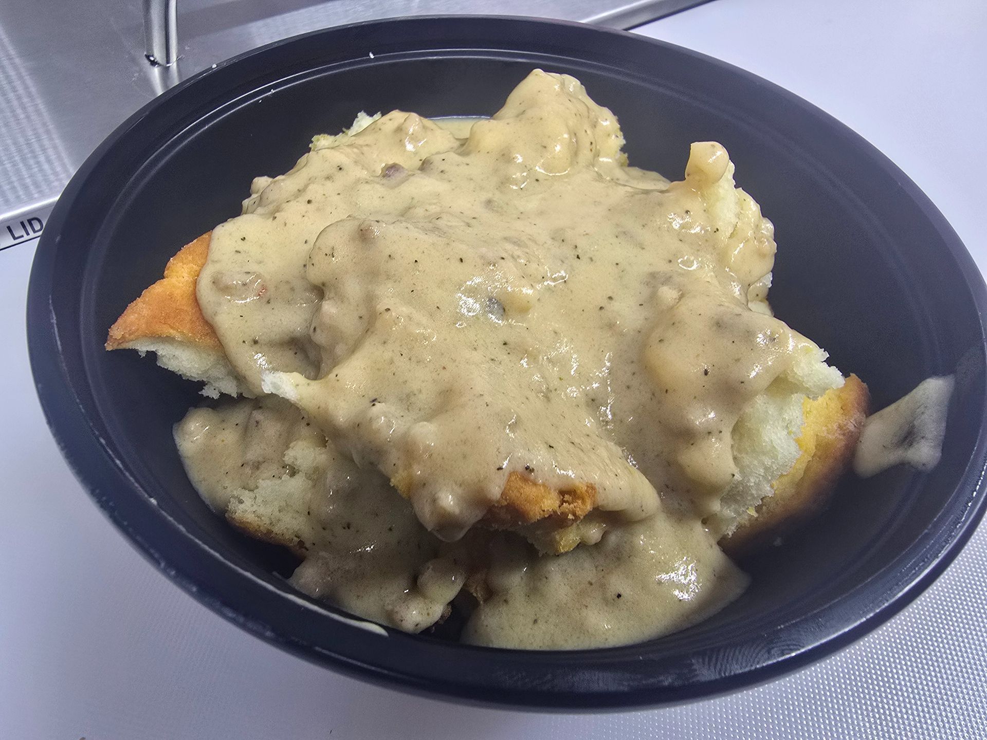 Black bowl of fried food covered in creamy white gravy on a tray
