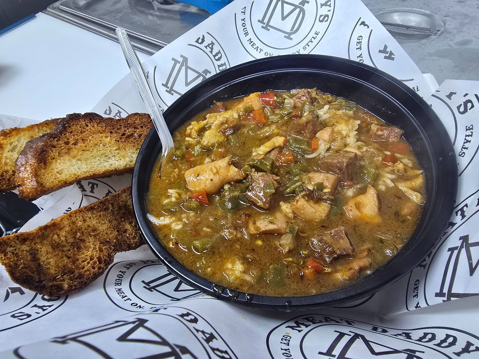 Bowl of chunky soup with two toasted bread slices on branded paper wrapper.
