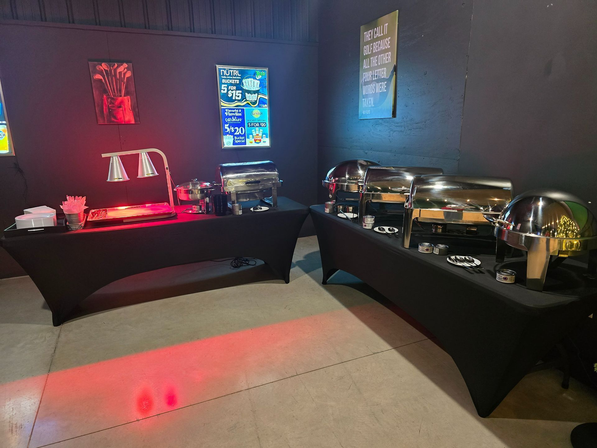 Buffet setup with black tablecloths, warm red and blue lighting, and multiple serving dishes in a dark room
