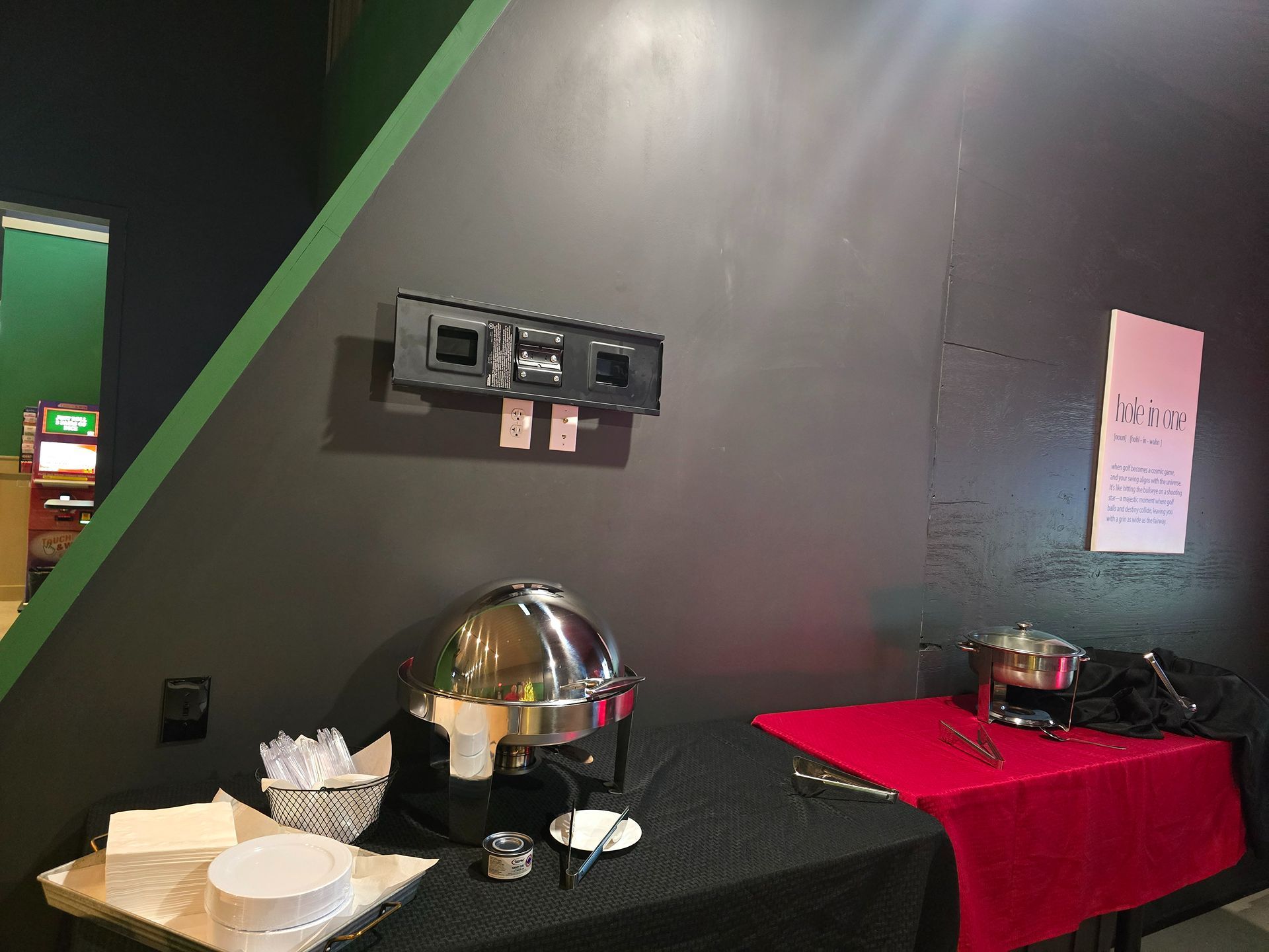 Buffet setup with covered serving dishes and plates on a black table beside a red tablecloth.
