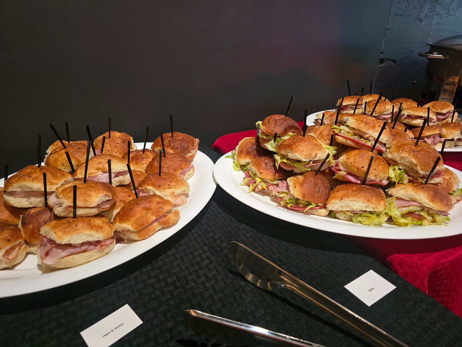 Two platters of mini sandwiches with toothpicks on a dark table, ready for serving
