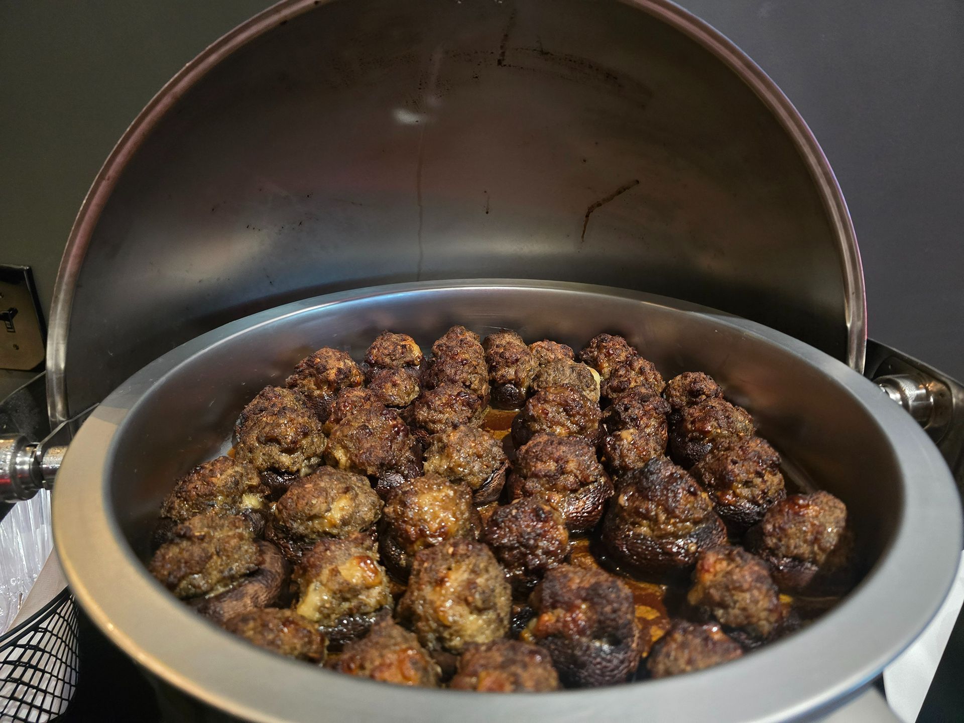 Large pot filled with browned meatballs or fritters cooking under a domed lid
