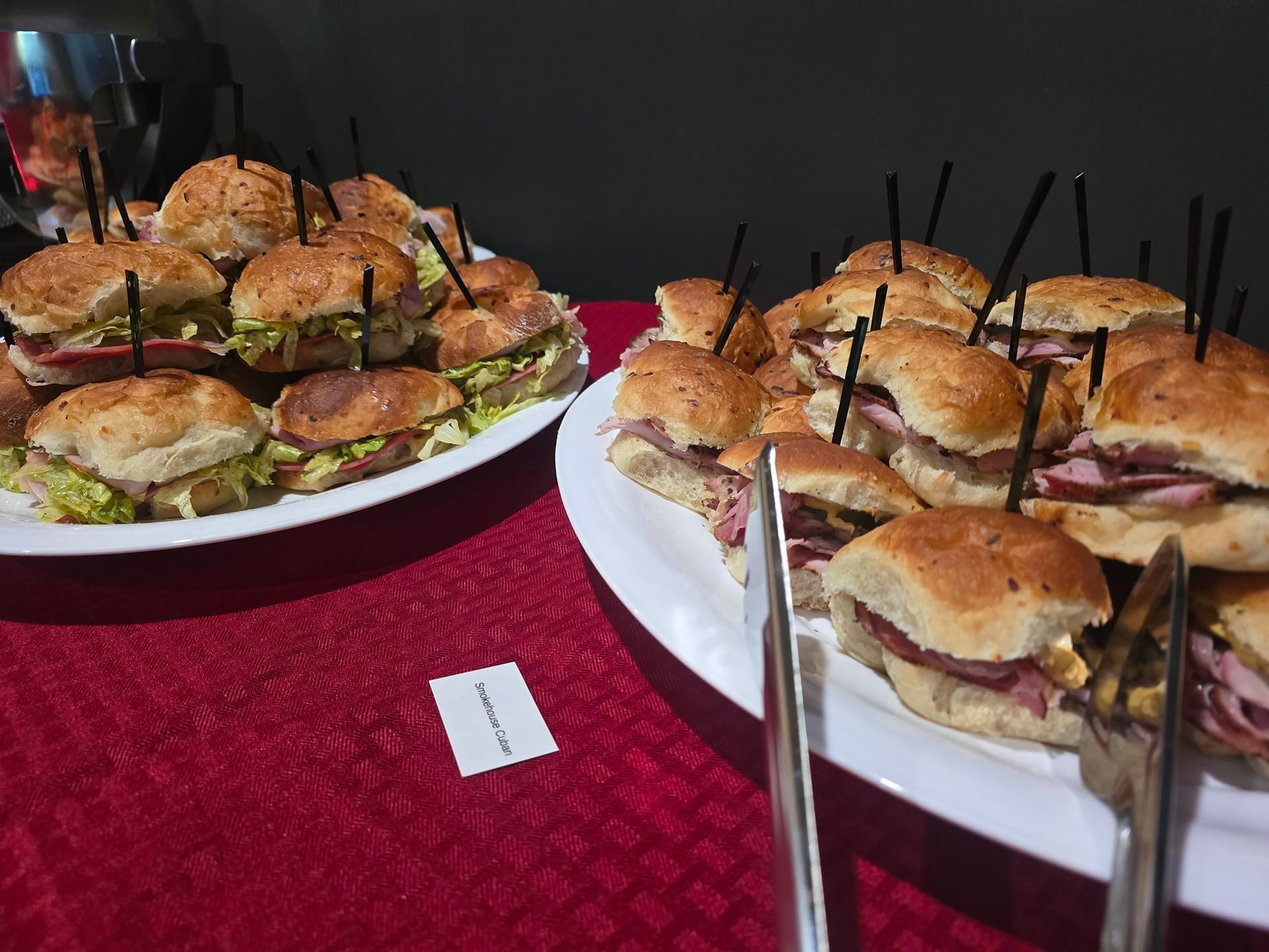 Plates of mini sandwiches on a red tablecloth, each held with black picks.