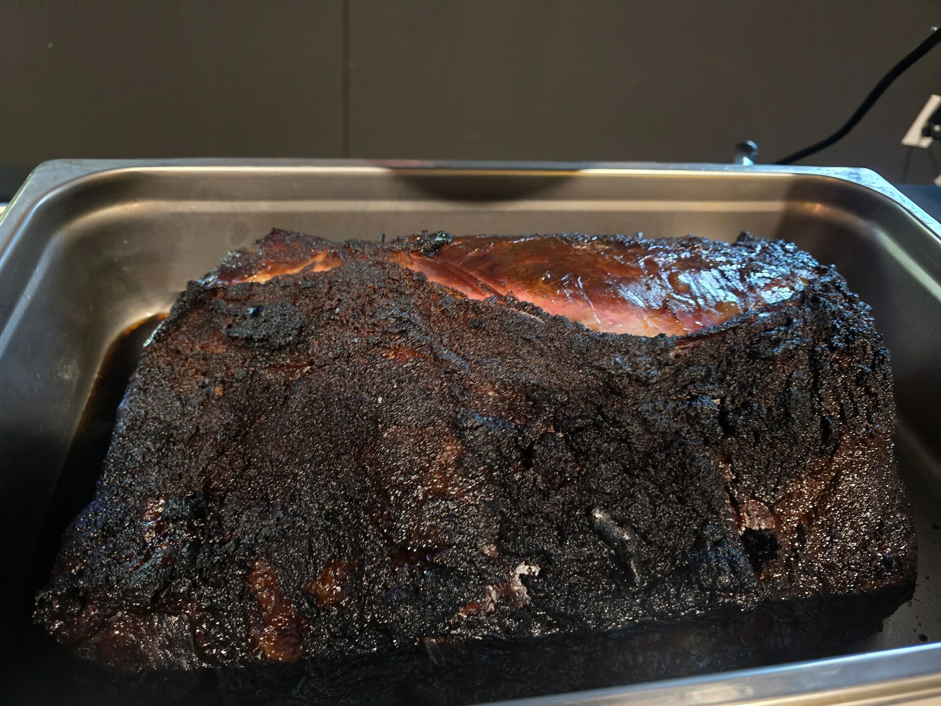Charred smoked meat brisket in a metal tray with a dark crust and glossy top