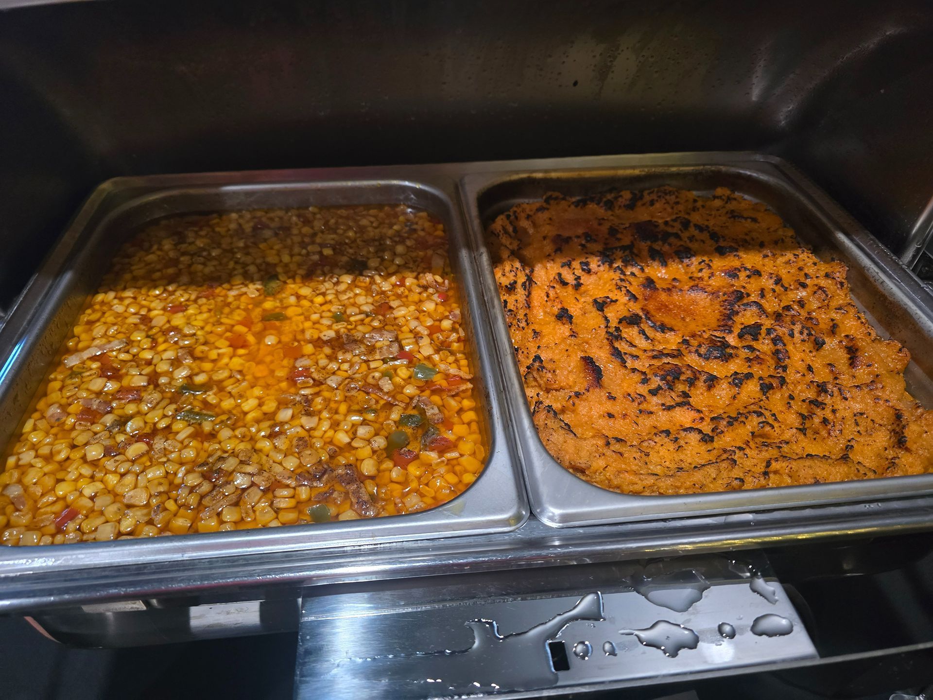 Two metal trays of cooked food, one brown and one orange, in a buffet-style warmer