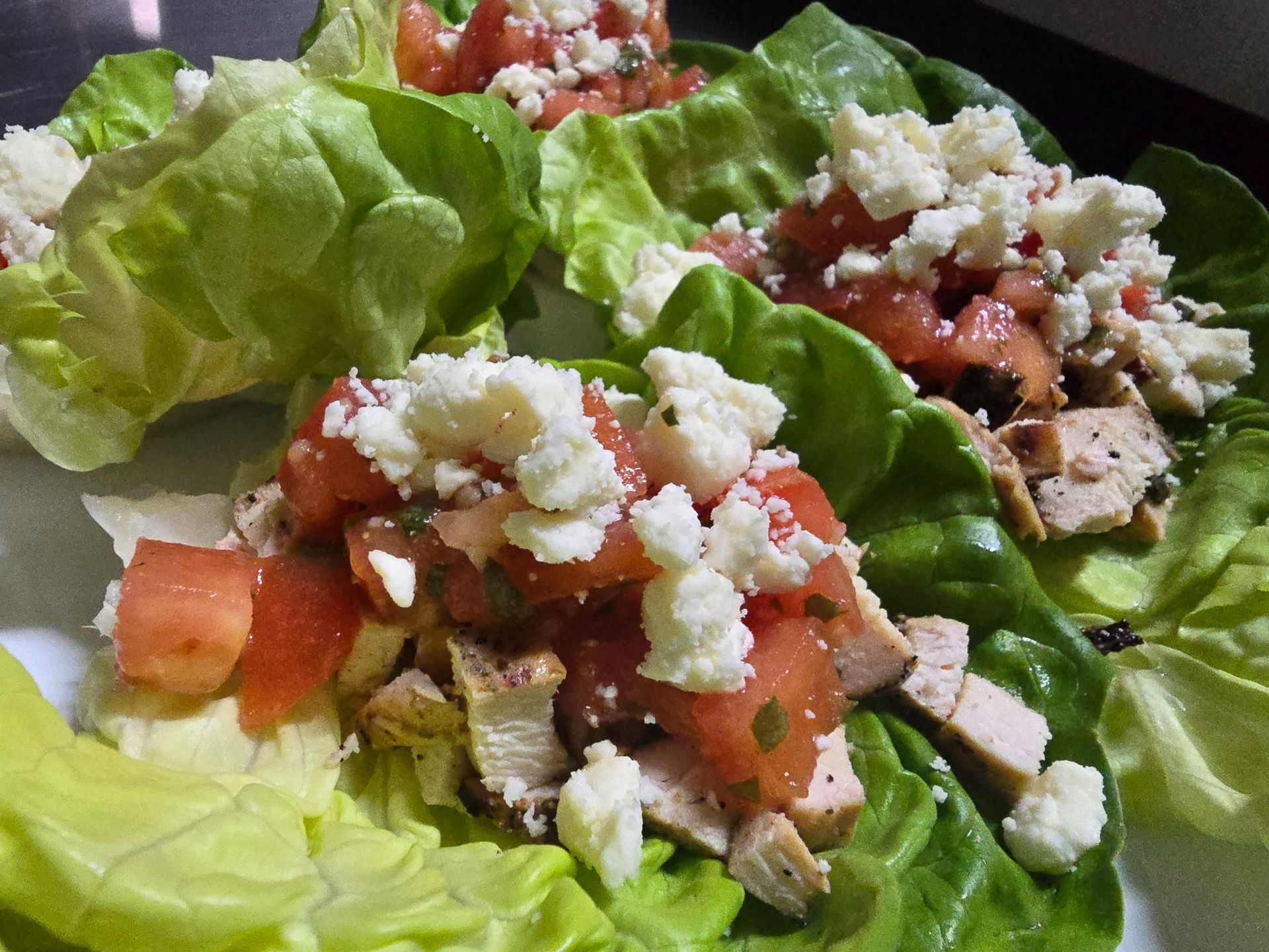 Lettuce cups filled with diced tomato, meat, and crumbled cheese on a plate
