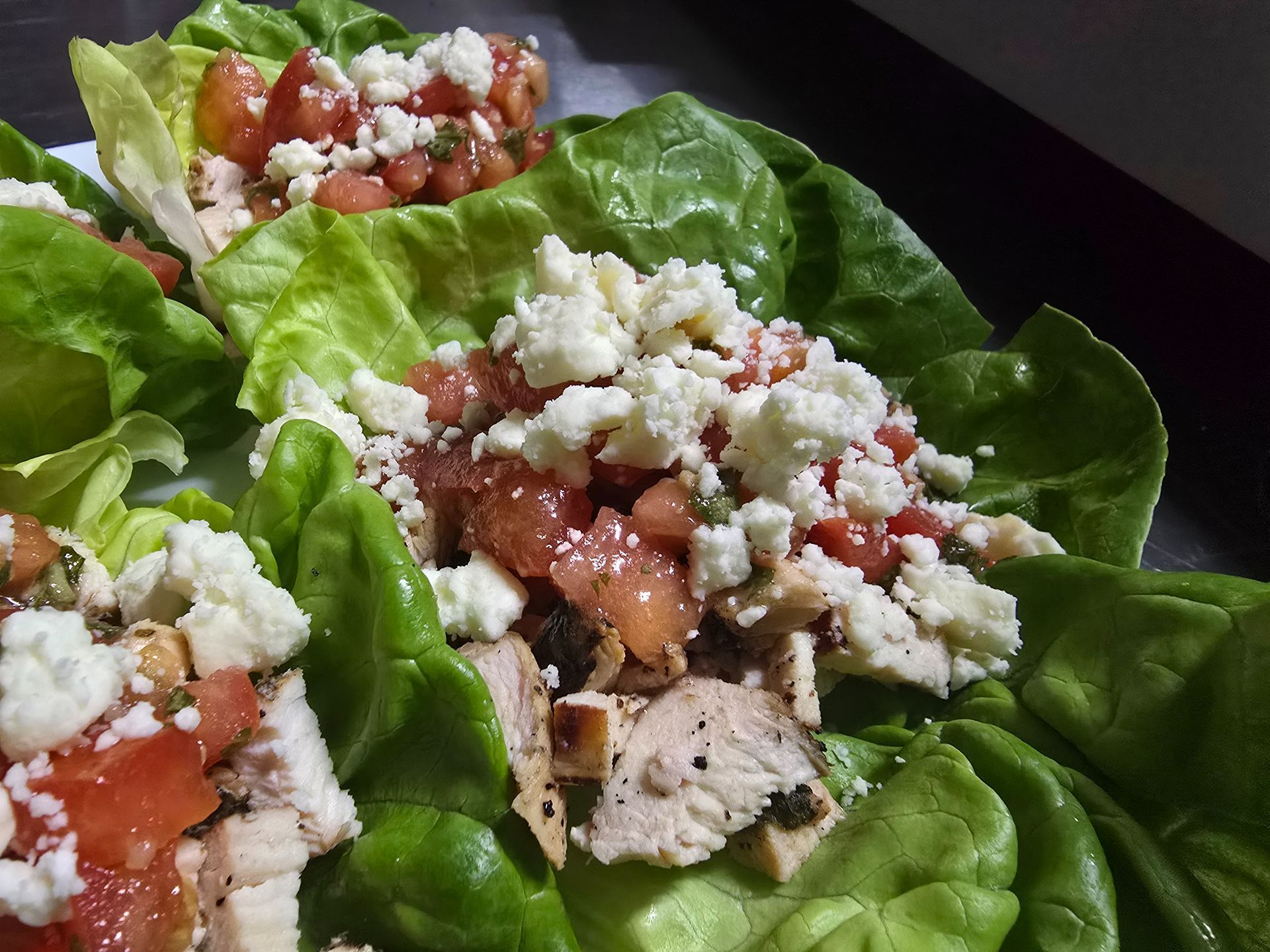 Lettuce wraps with diced tomatoes, crumbled cheese, and grilled chicken on a plate