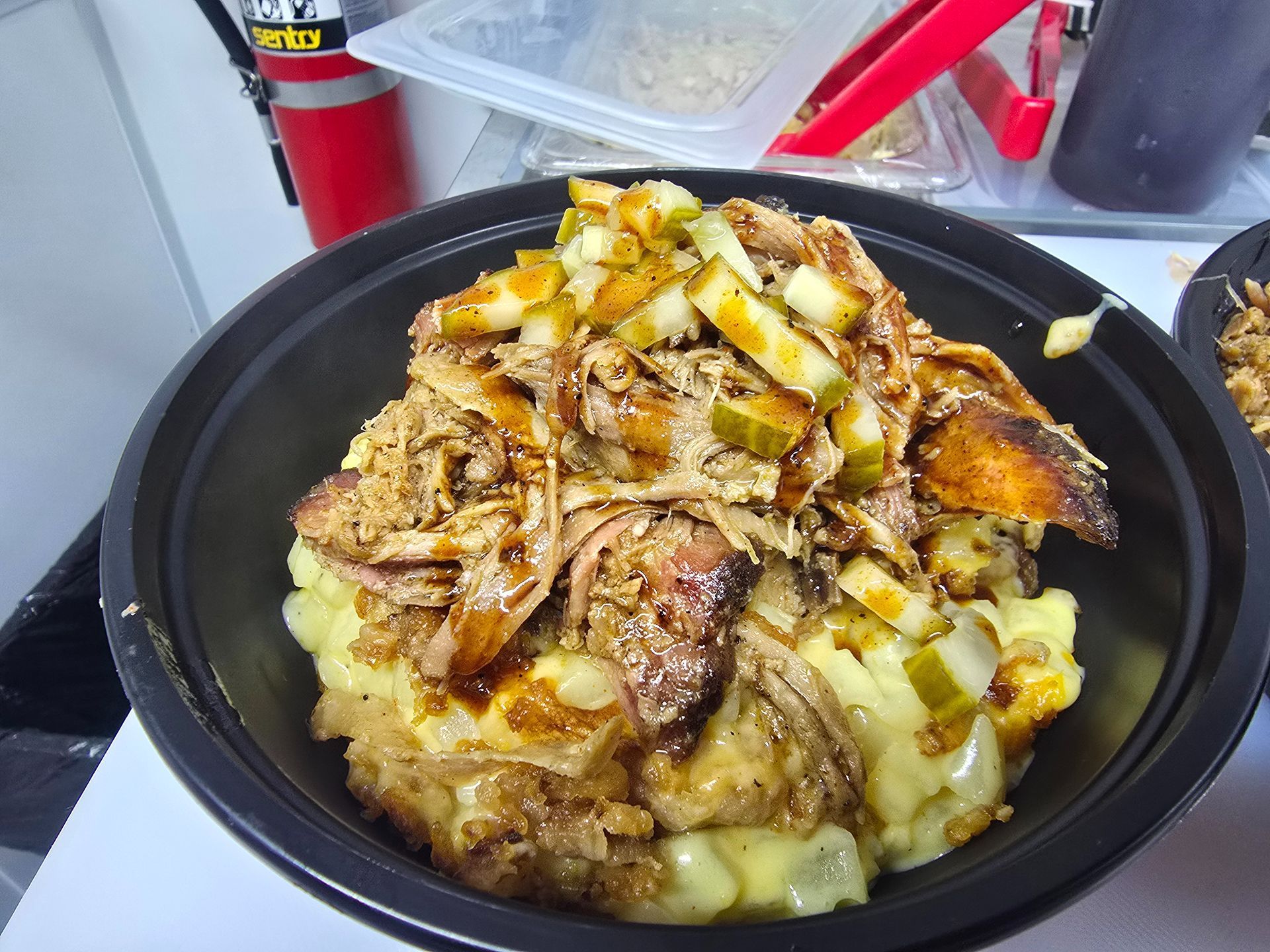 Black bowl of chopped food topped with sauce and meat on a stovetop counter