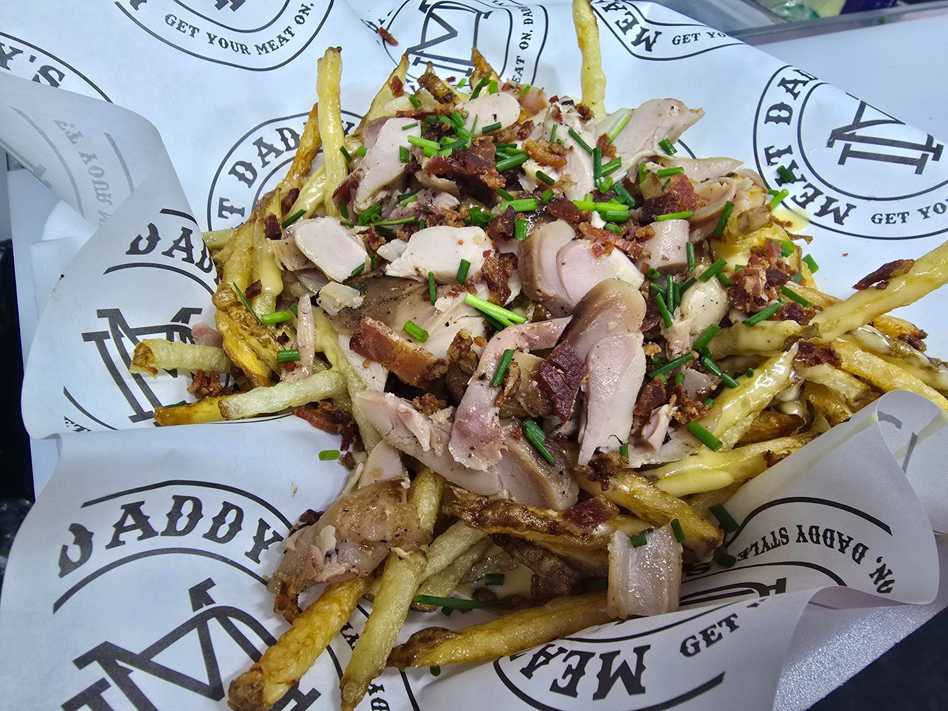 French fries topped with chopped meat and herbs in a paper-lined basket
