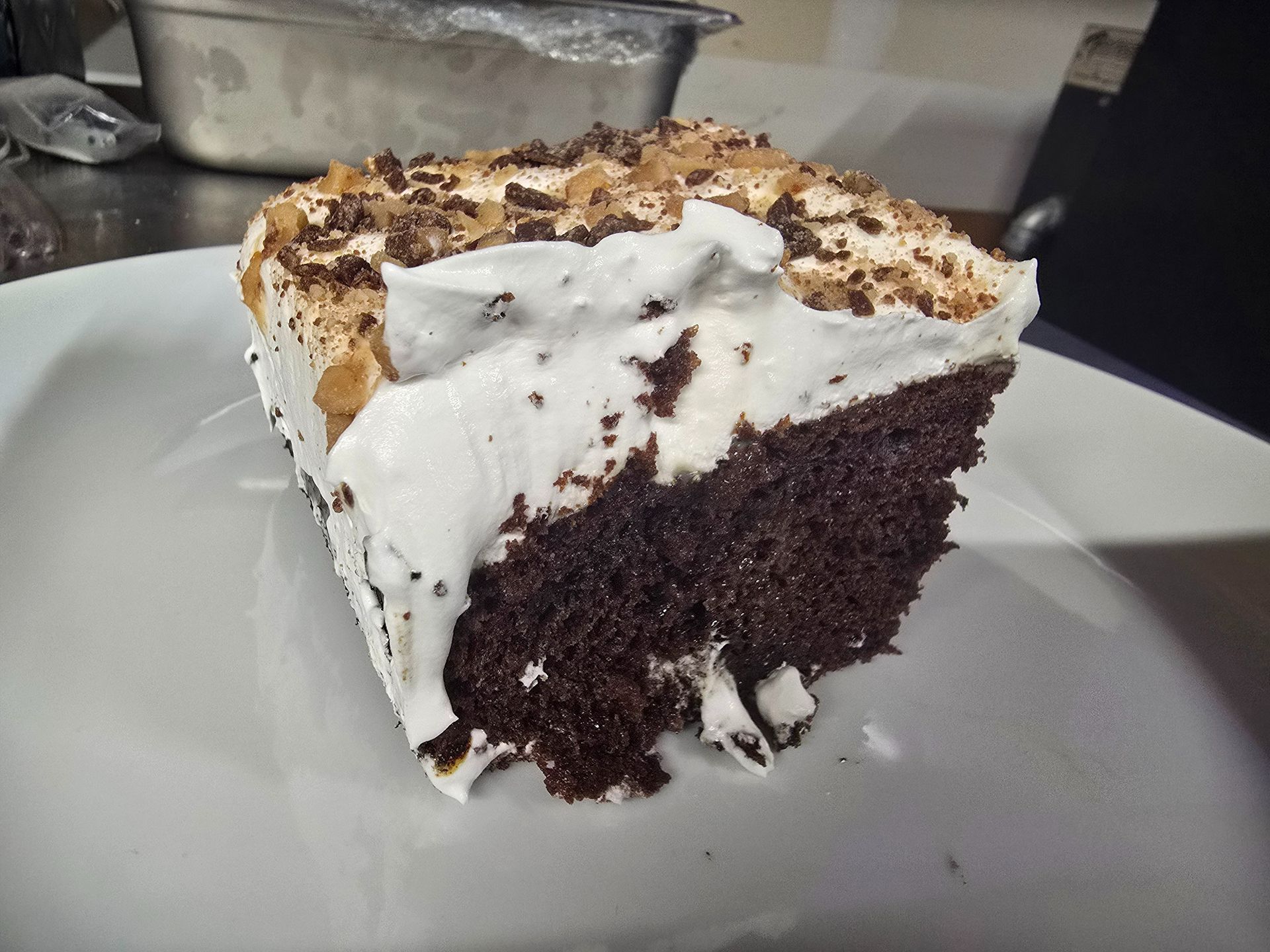 Slice of chocolate cake with white frosting and crumb topping on a white plate