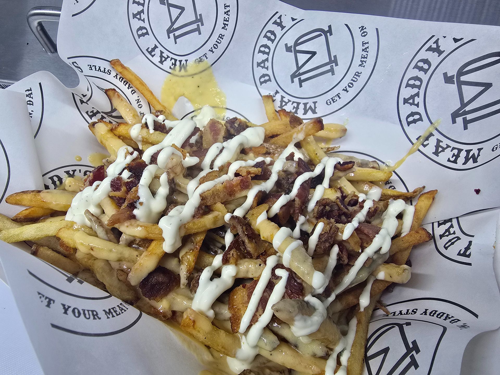 Loaded fries topped with beef, melted cheese, and white sauce on branded paper