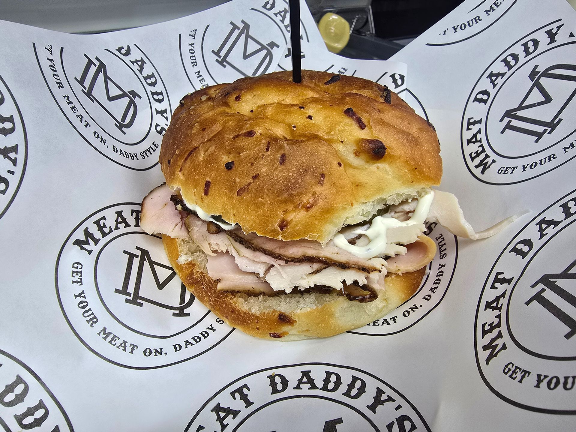Sandwich with melted cheese on branded paper wrapping, topped with a toasted bun.