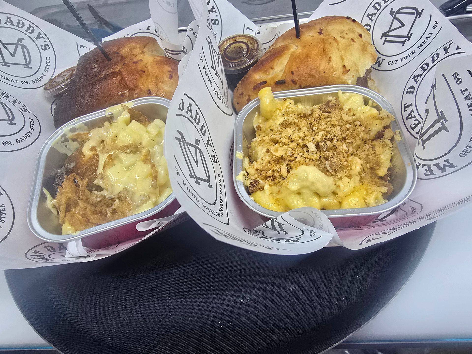 Two takeout bowls of rice and roasted chicken on a black tray with branded paper liners