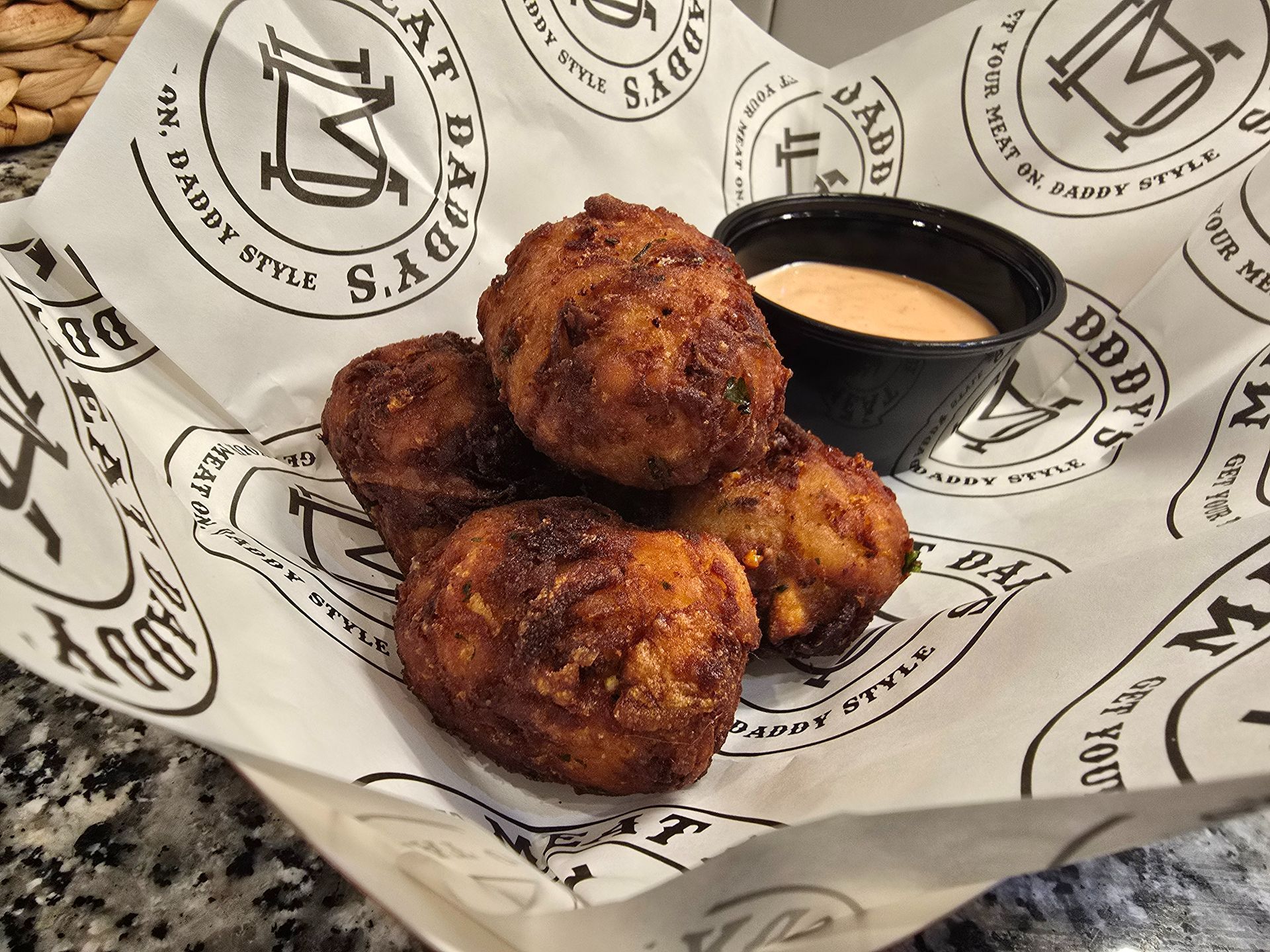 Basket of fried croquettes with dipping sauce on branded paper lining