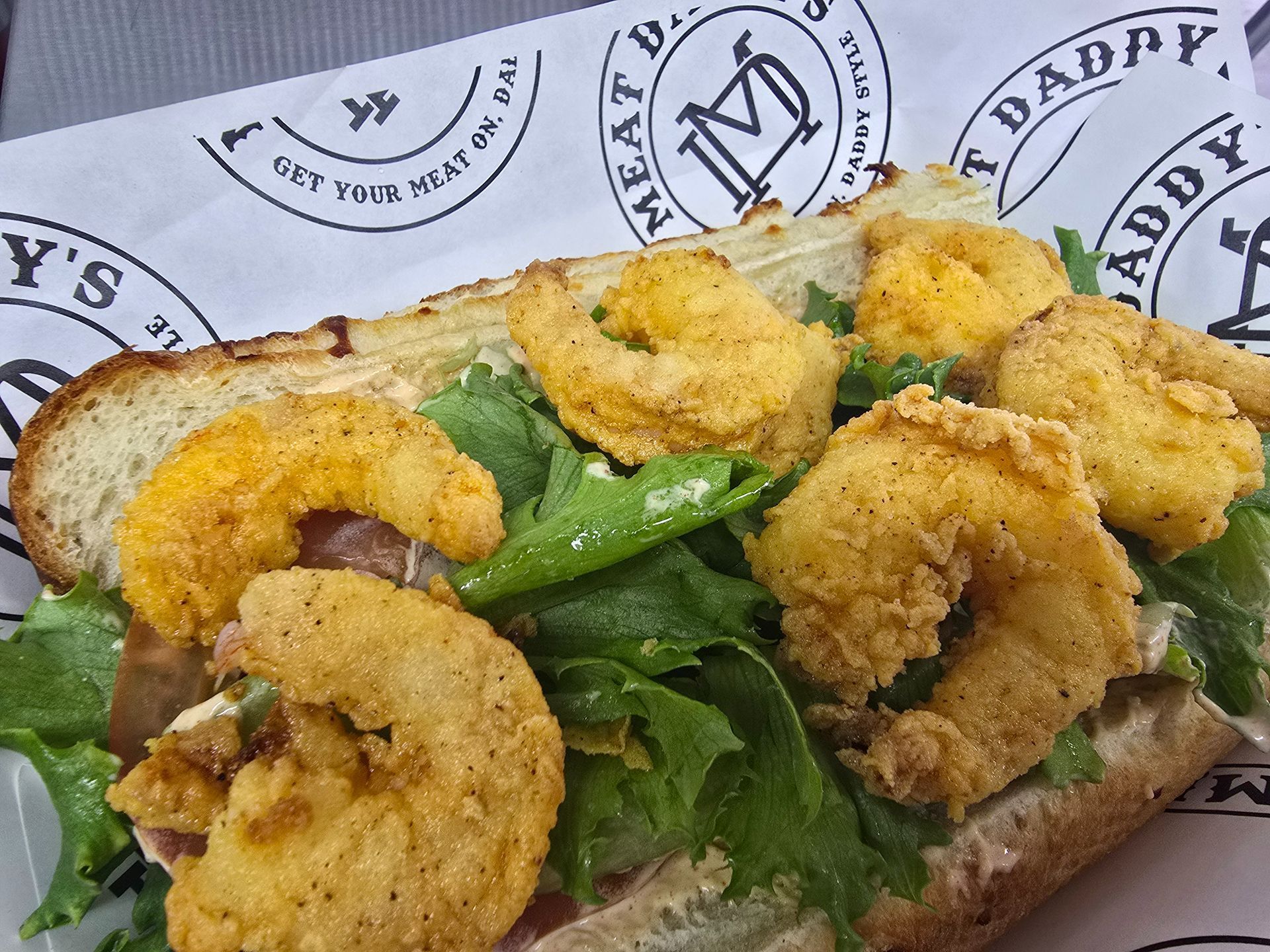 Open-faced sandwich topped with fried shrimp, greens, and green peppers on rustic bread