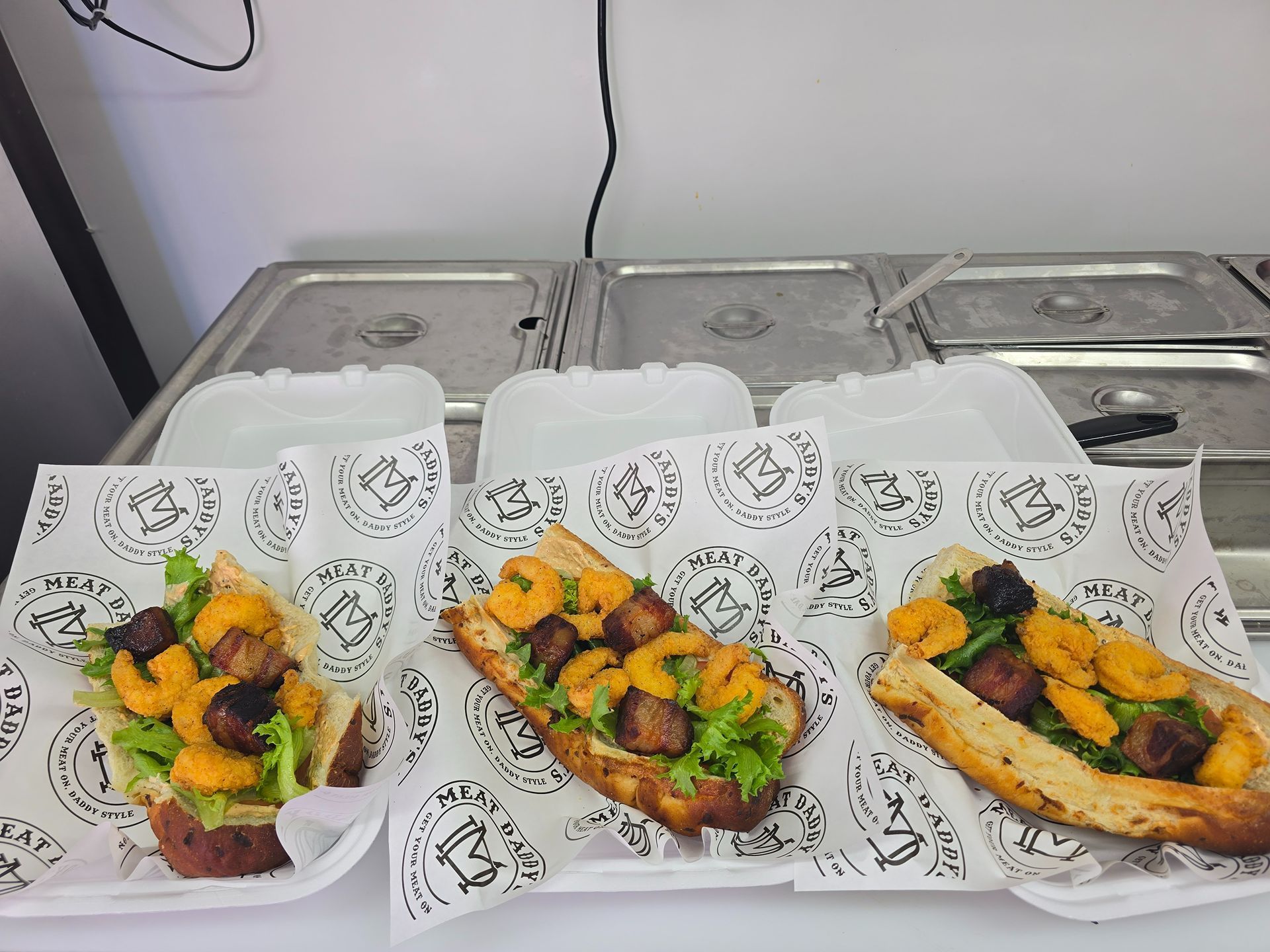 Three takeout wraps with grilled chicken and vegetables on patterned paper in white plastic trays