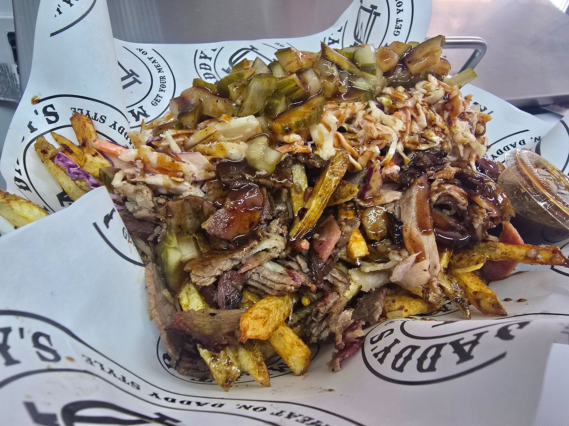 Tray of loaded fries topped with cheese, sauce, and chopped vegetables on branded paper liner