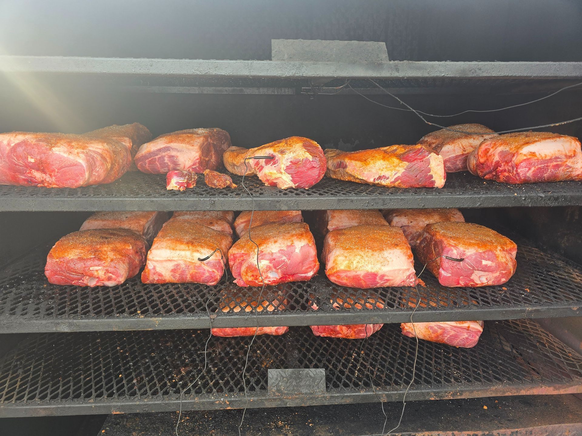 Smoked meat pieces on a grill rack, with golden-brown and red glazed surfaces.