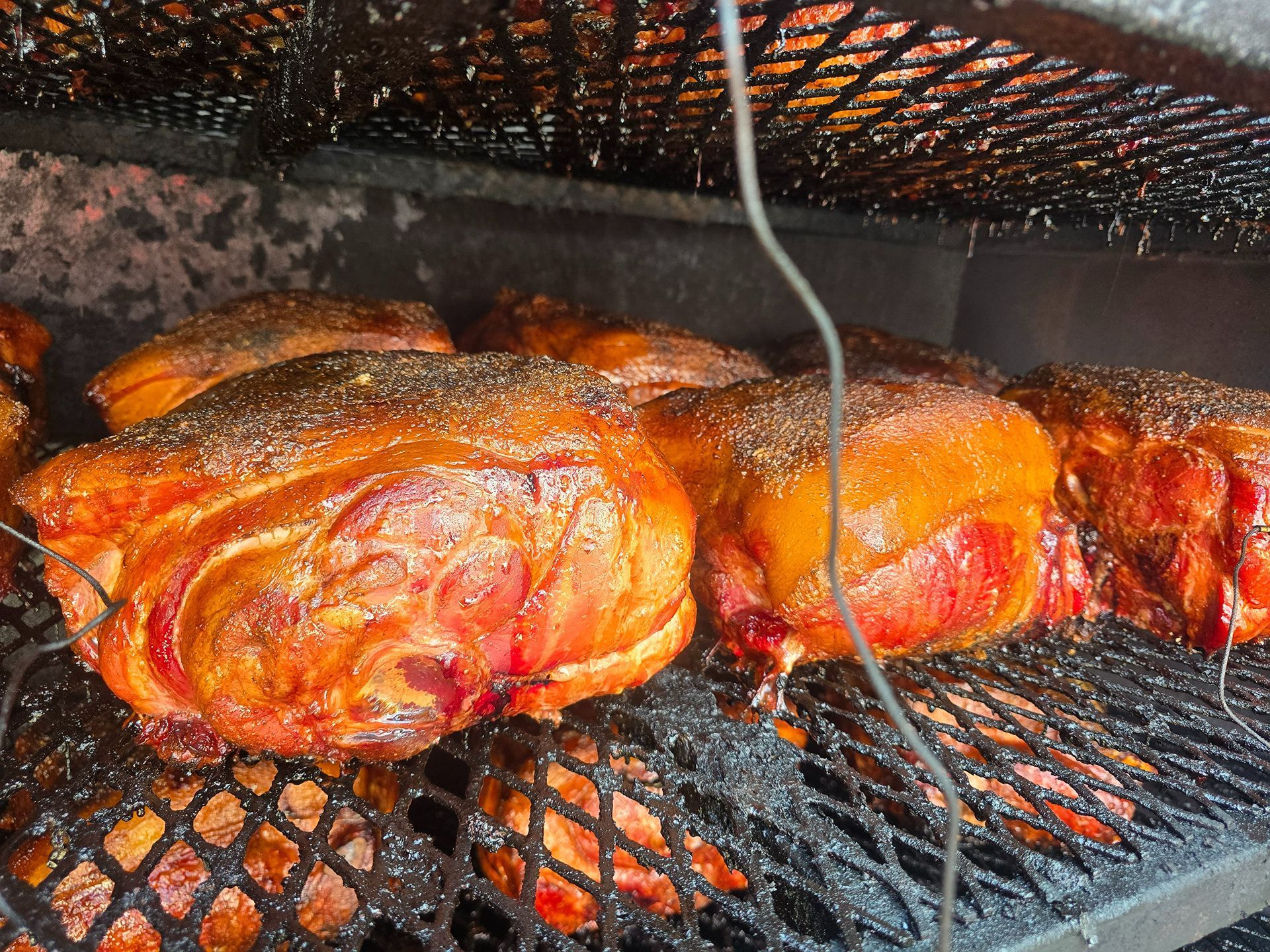Whole roasted chickens sizzling on a grill, coated in reddish-orange seasoning under a wire rack