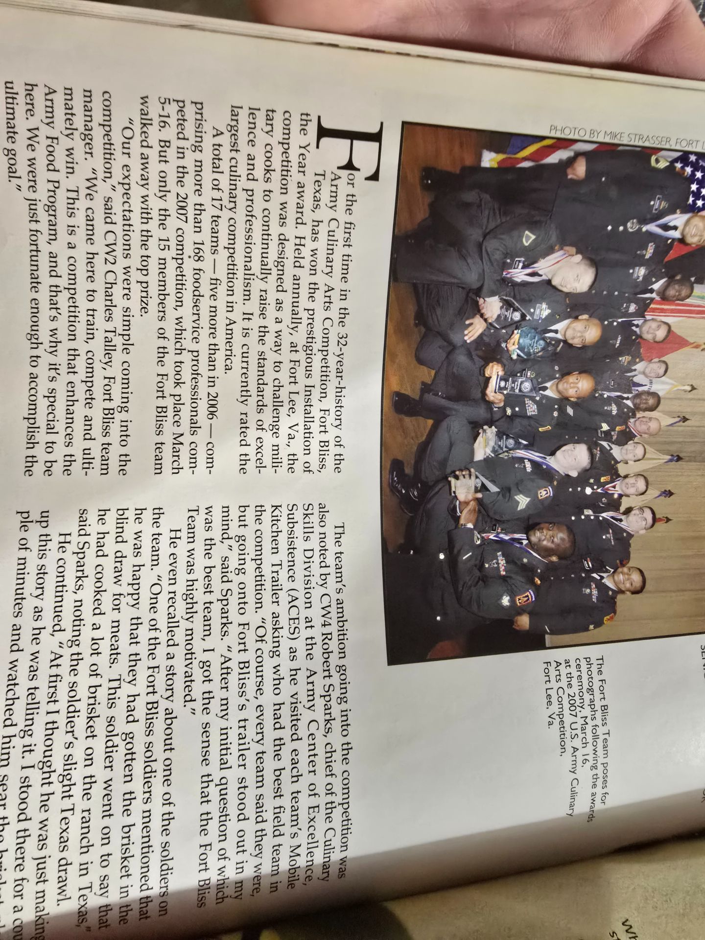 Rotated magazine page with a group photo of people in dark suits above dense columns of text.