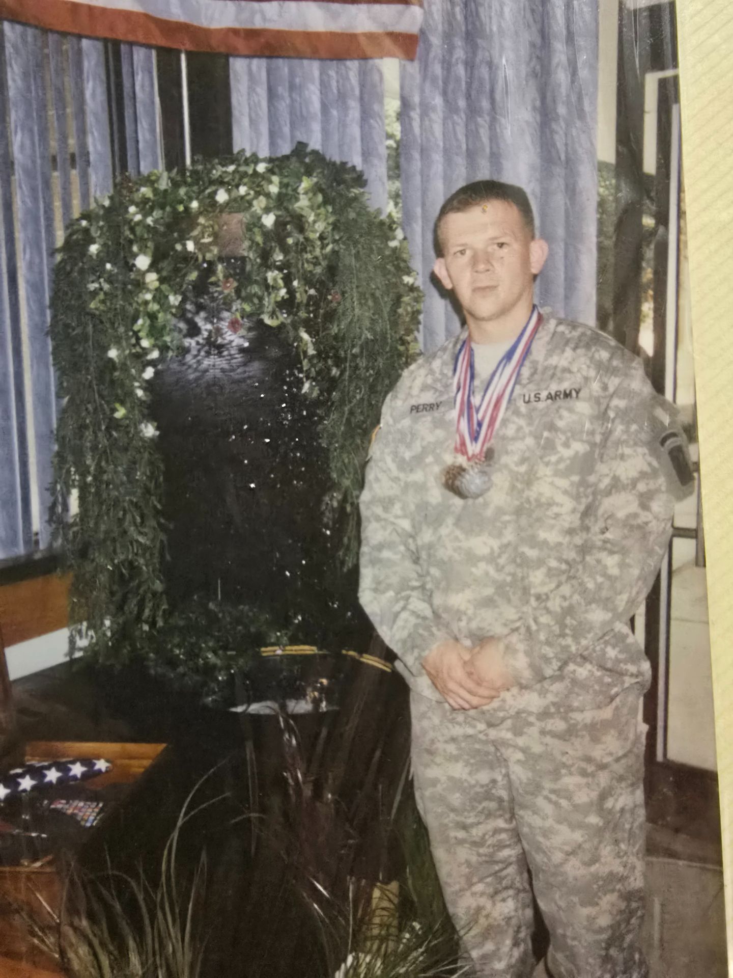 Person in military camouflage uniform standing indoors with medals around their neck.