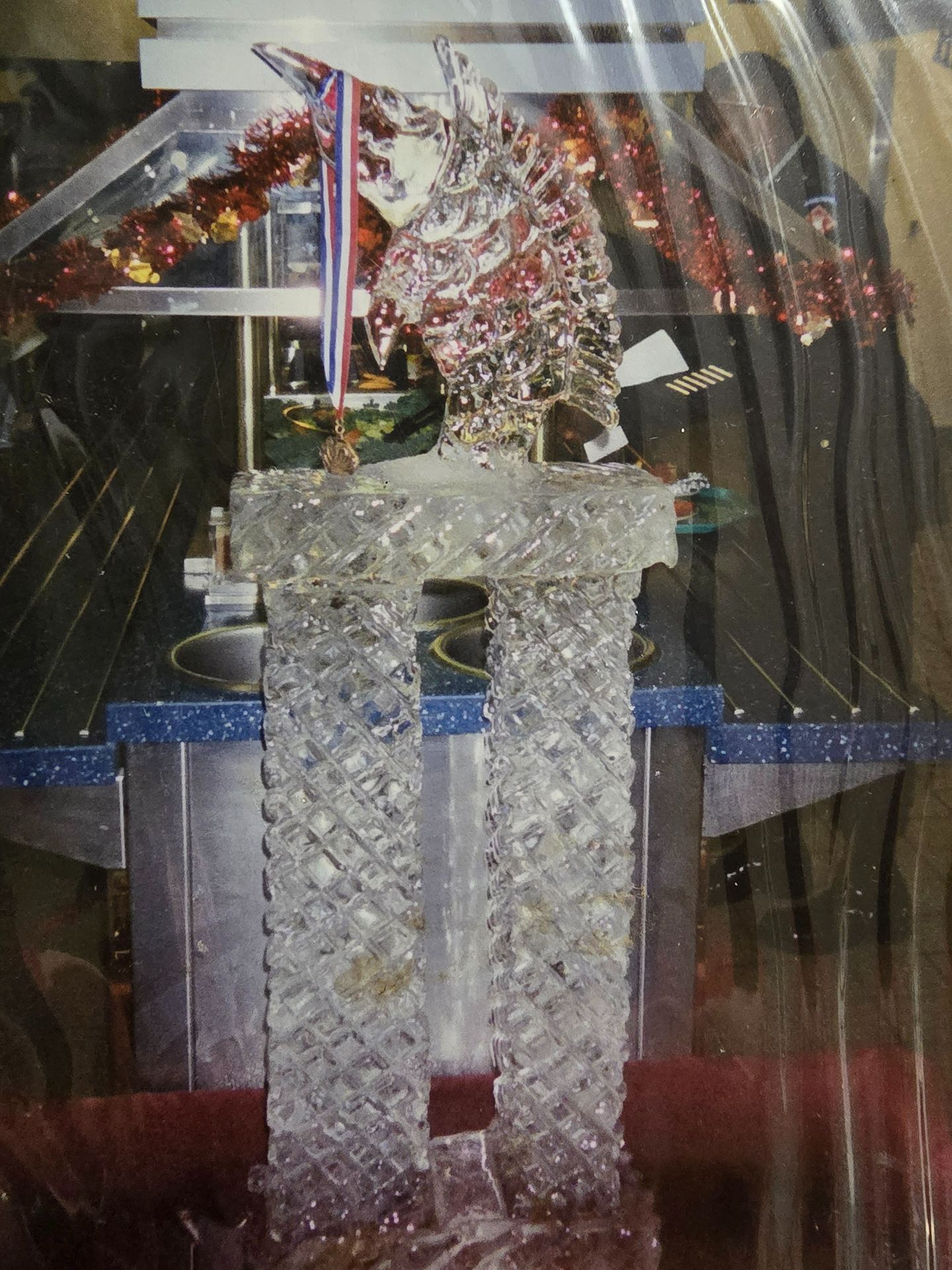 Clear crystal trophy on a red backdrop, topped with a decorative silver and red figure.