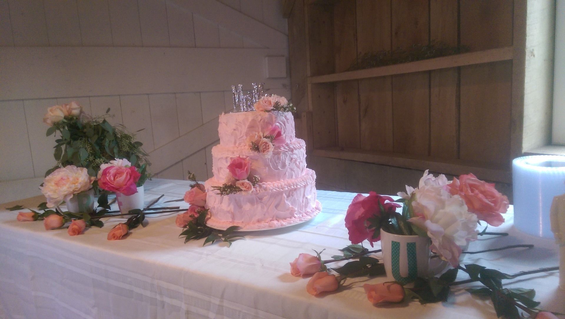 Pink tiered cake centerpiece on a decorated table with flowers and rose petals in a wooden room