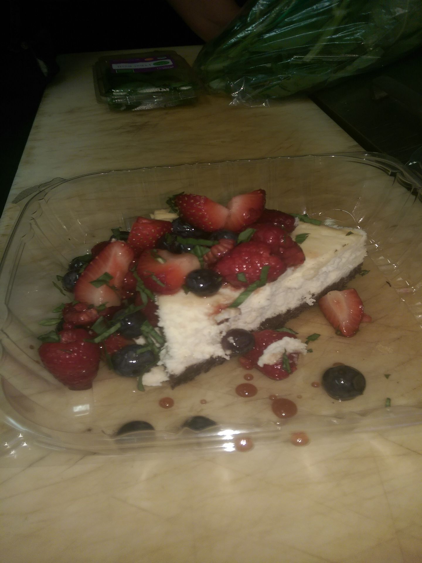 Dessert slice topped with strawberries and blueberries in a clear plastic container on a table