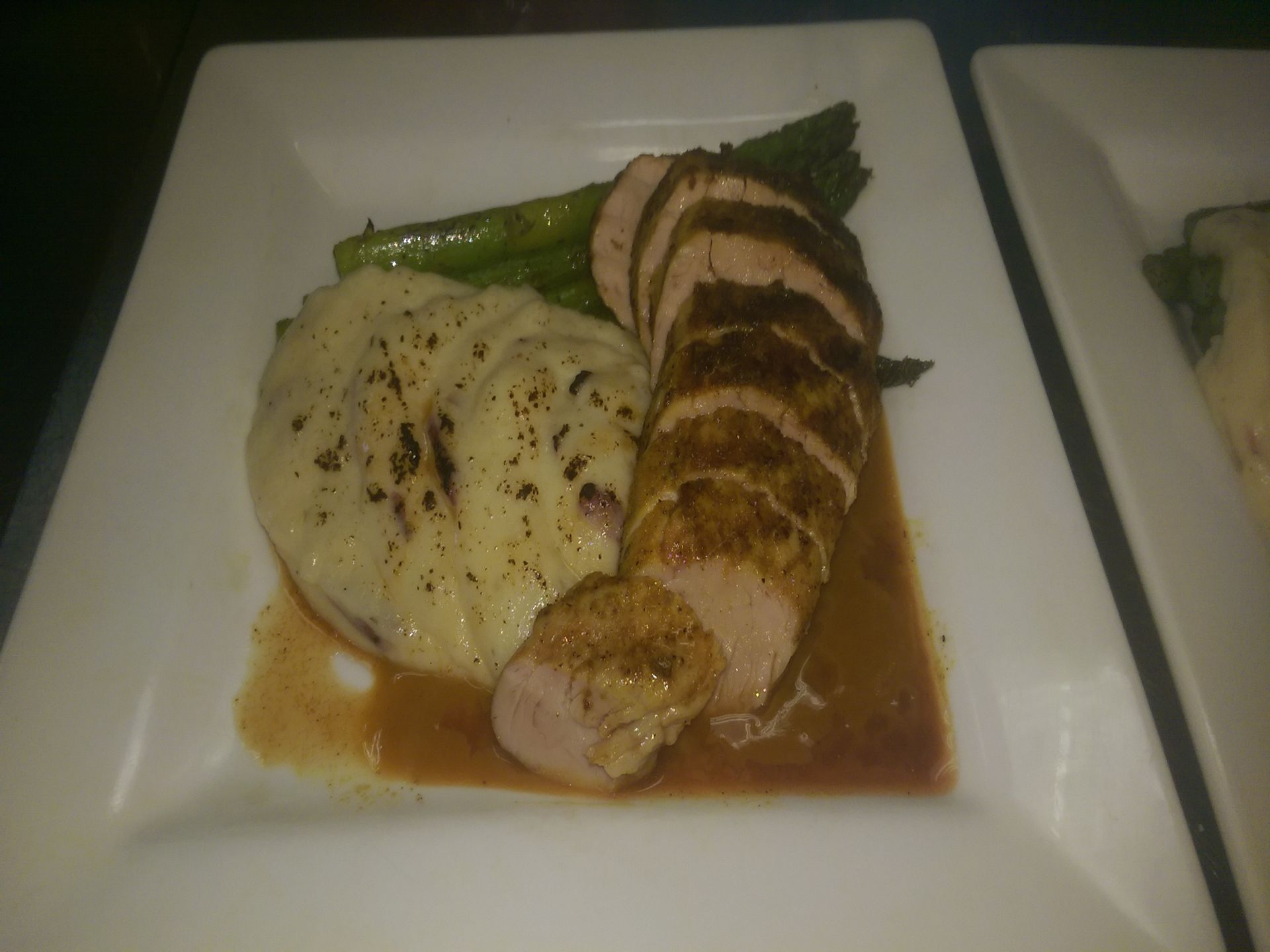 Plated sliced chicken with mashed potatoes, green beans, and sauce on a white square dish
