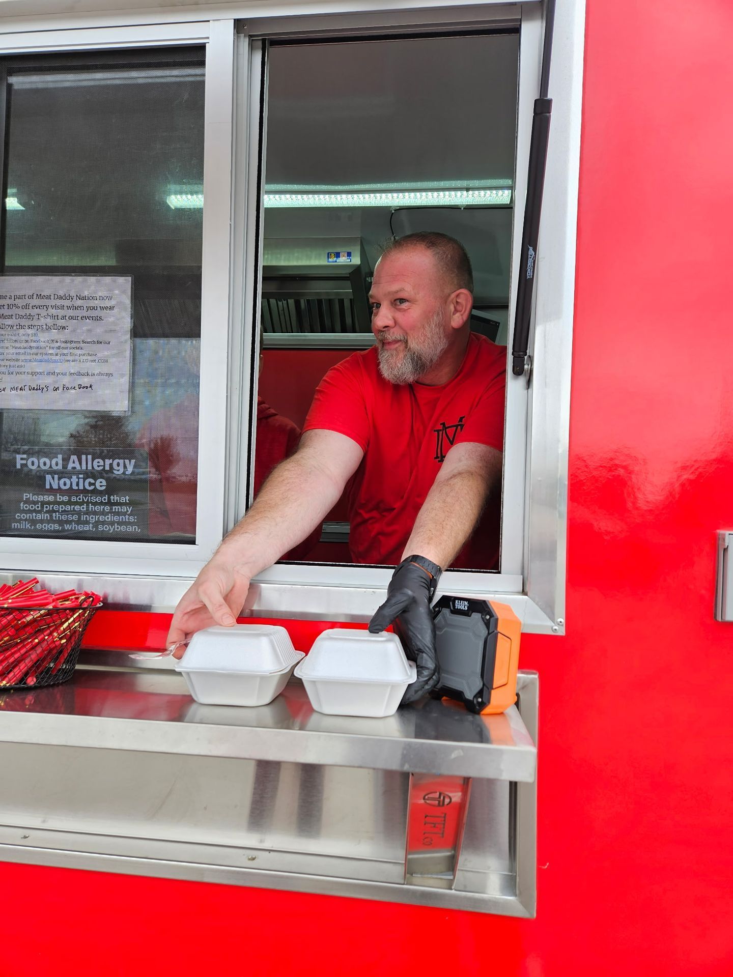 Food truck worker in red shirt and black gloves handing out takeout containers from service window