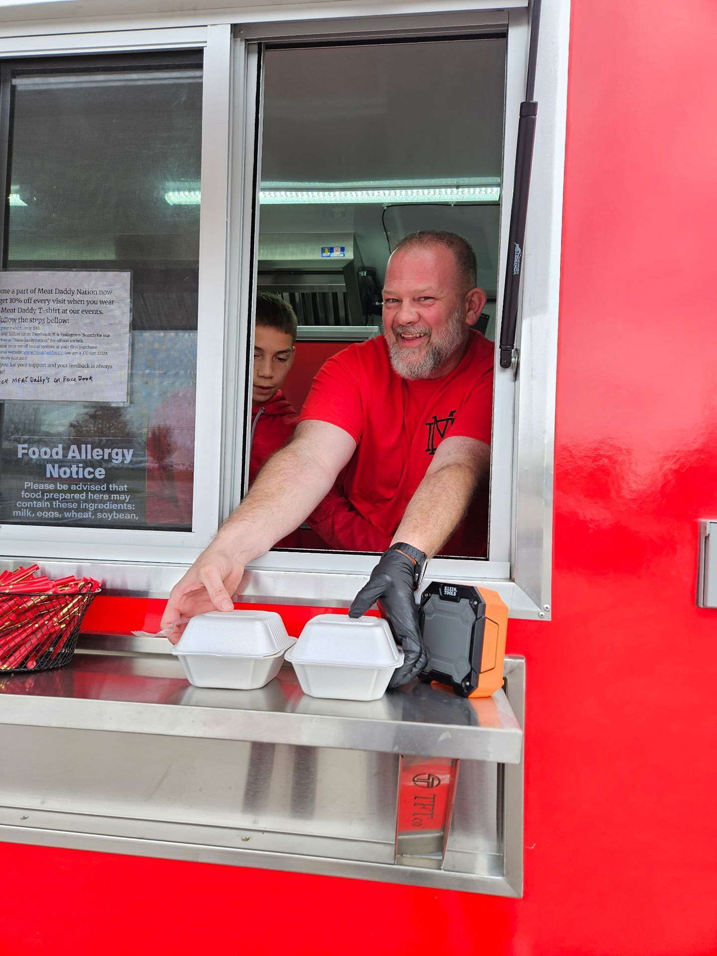 Food truck worker in red shirt handing out takeout containers at the window