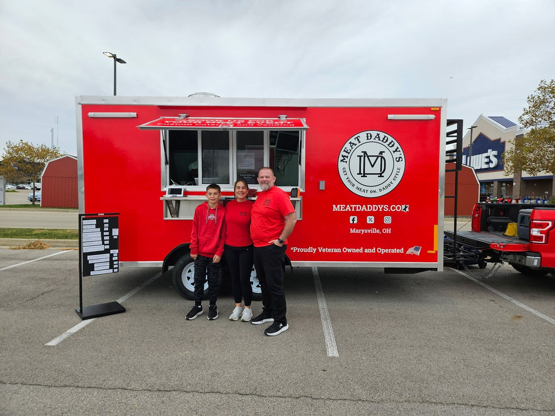 Two people in red shirts standing in front of a red food truck in a parking lot