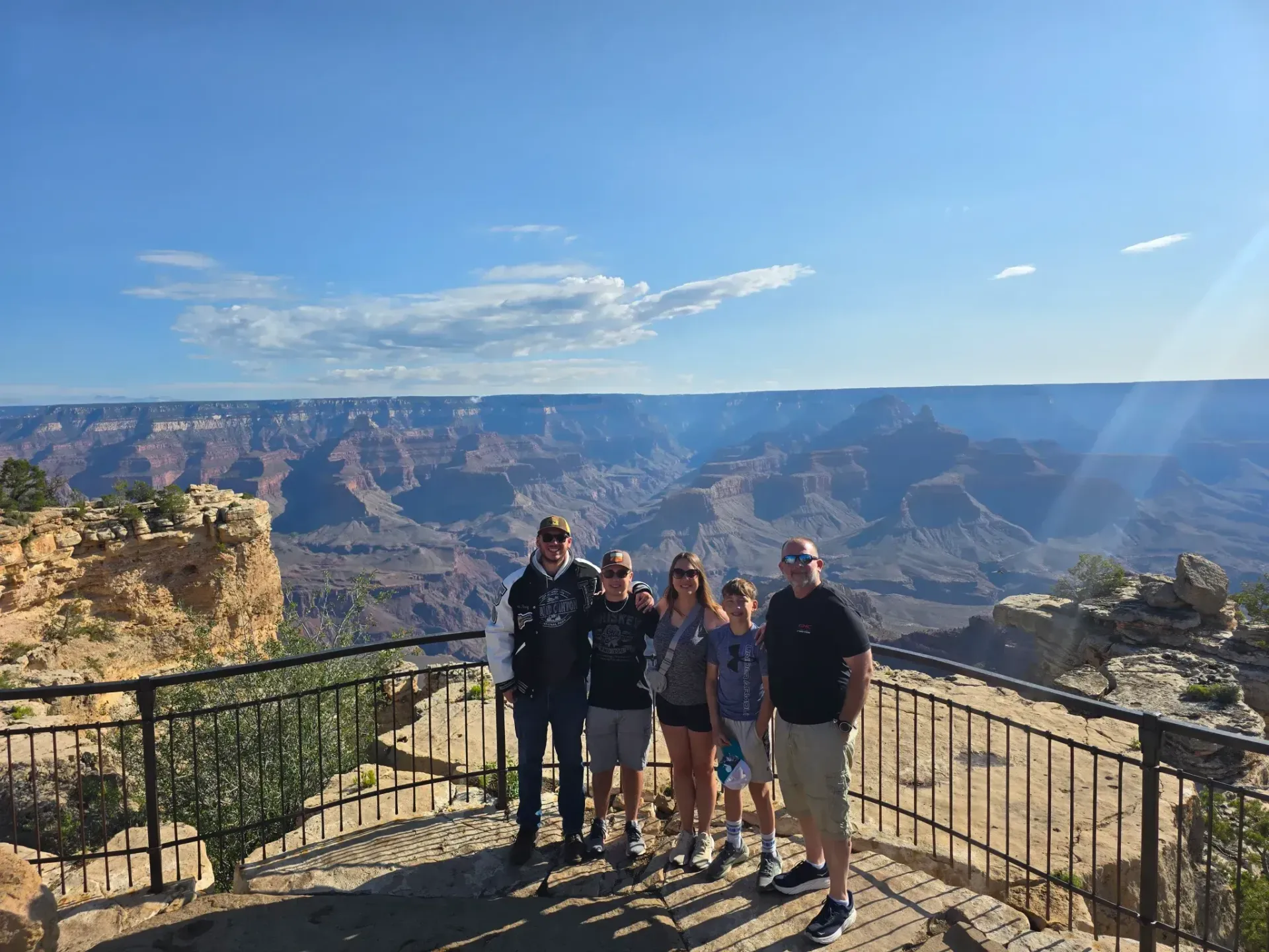 Five people posing at a Grand Canyon overlook with blue sky and canyon cliffs behind them