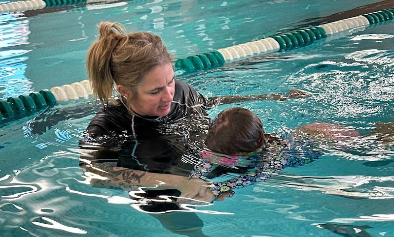 A young girl is receiving swim instruction from a female instructor.