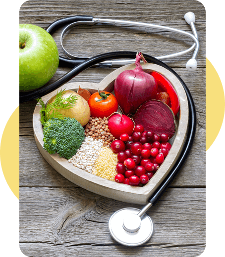 Heart-shaped bowl of colorful fruits and vegetables with a stethoscope on a wooden table