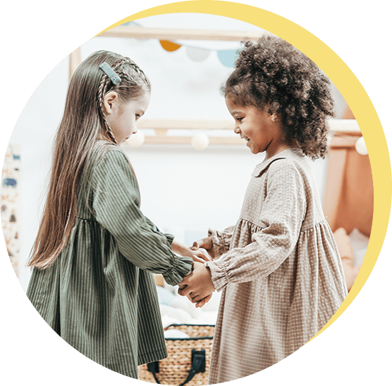 Two children holding hands indoors, smiling at each other in a bright playroom
