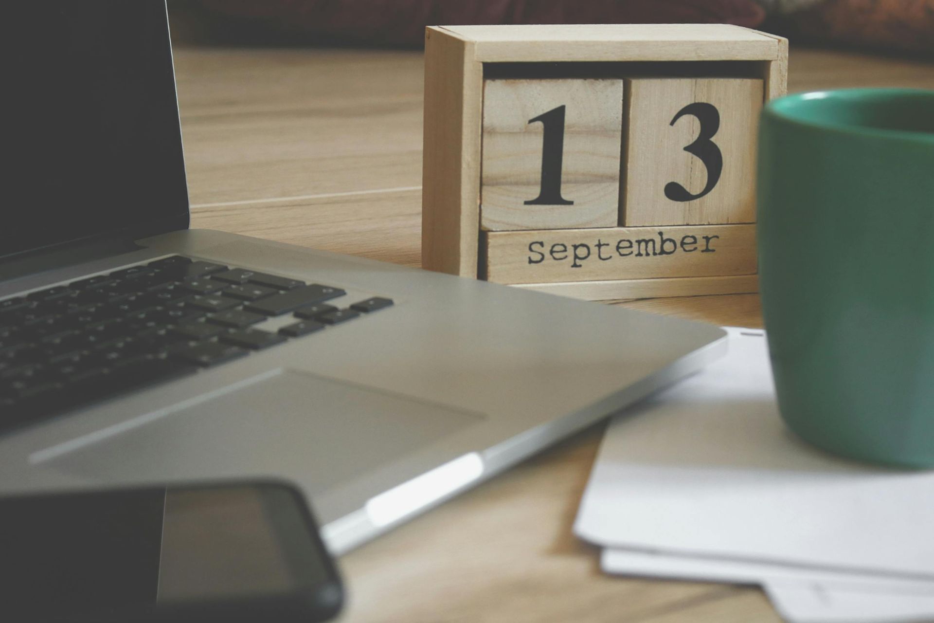 Laptop, phone, and coffee cup sit on a desk next to a wooden calendar reading September 13.