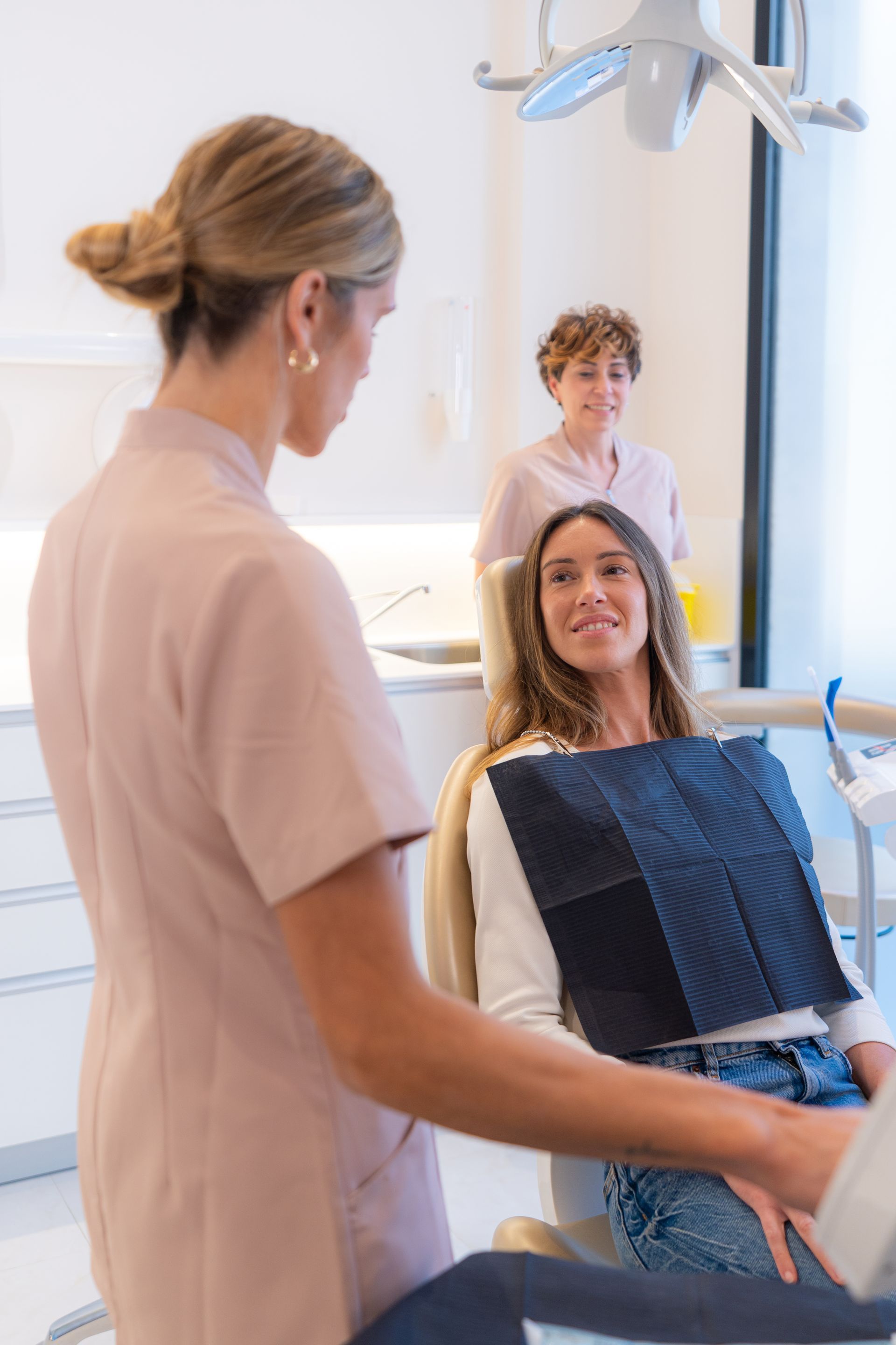 Dentist examining a patient in a dental chair; assistant stands nearby.