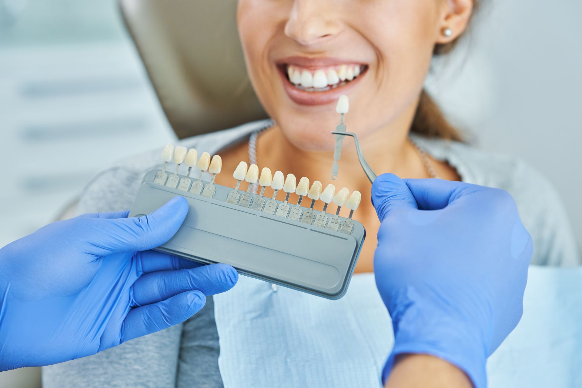 Dentist holding a shade guide next to a patient's teeth to determine tooth whitening level.