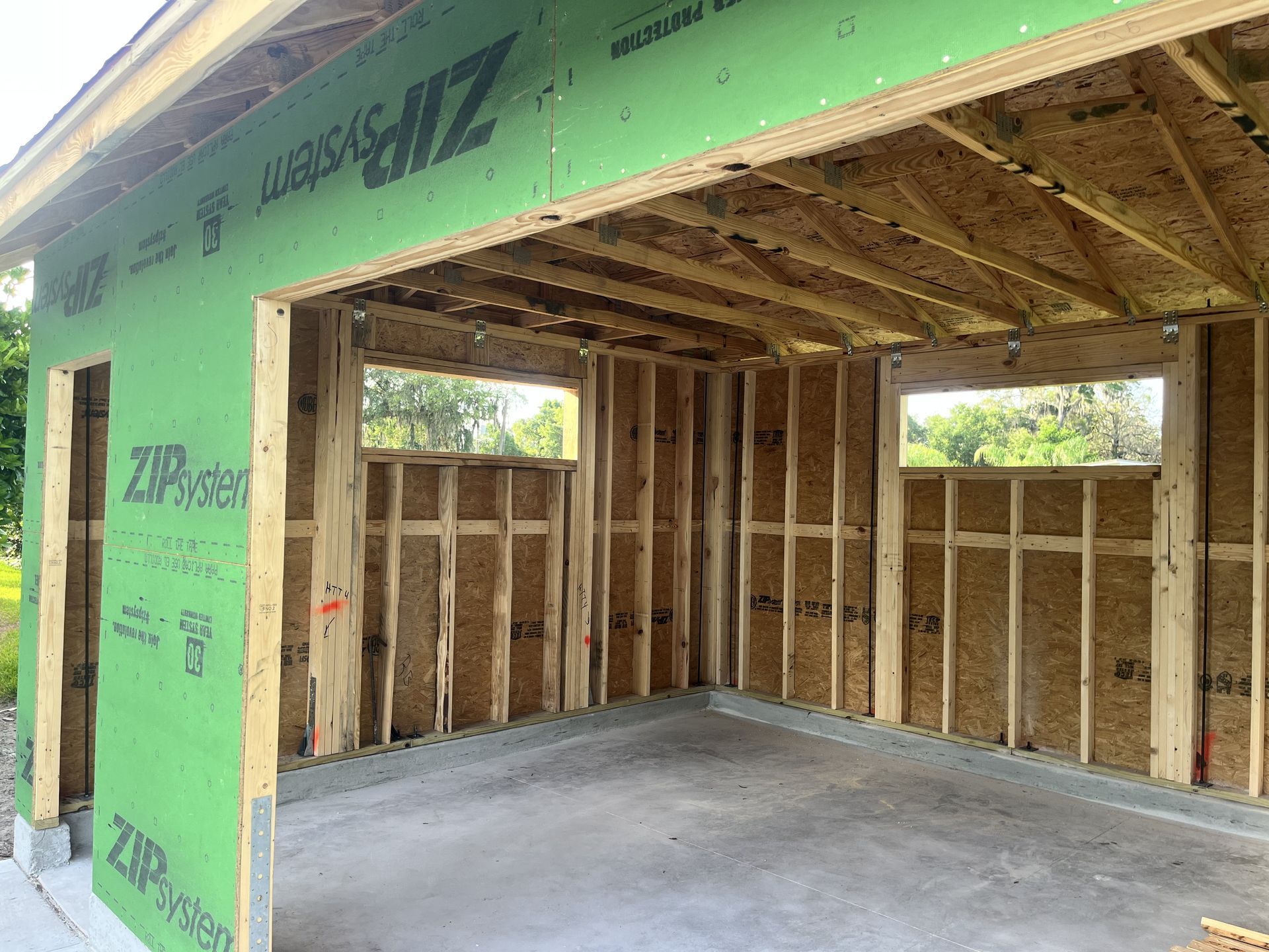 Framed garage under construction with green sheathing, exposed studs, and concrete floor