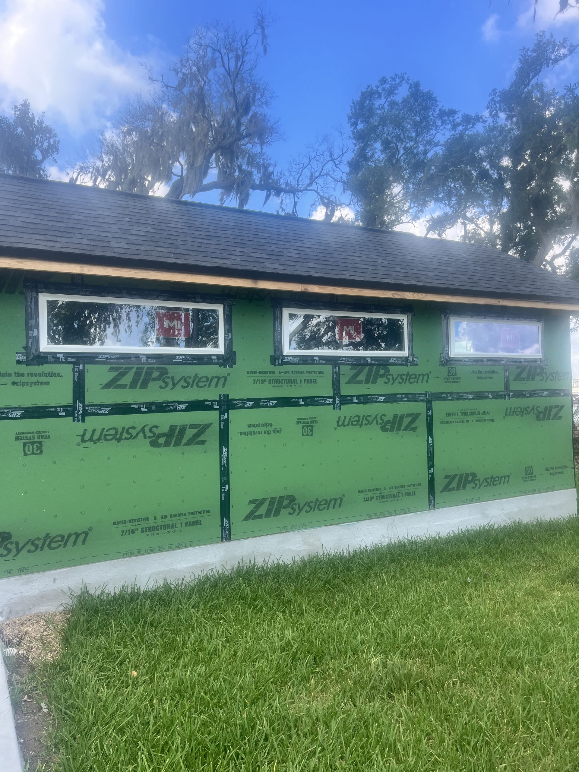Green Zip System exterior wall under construction beside a grassy yard and trees.