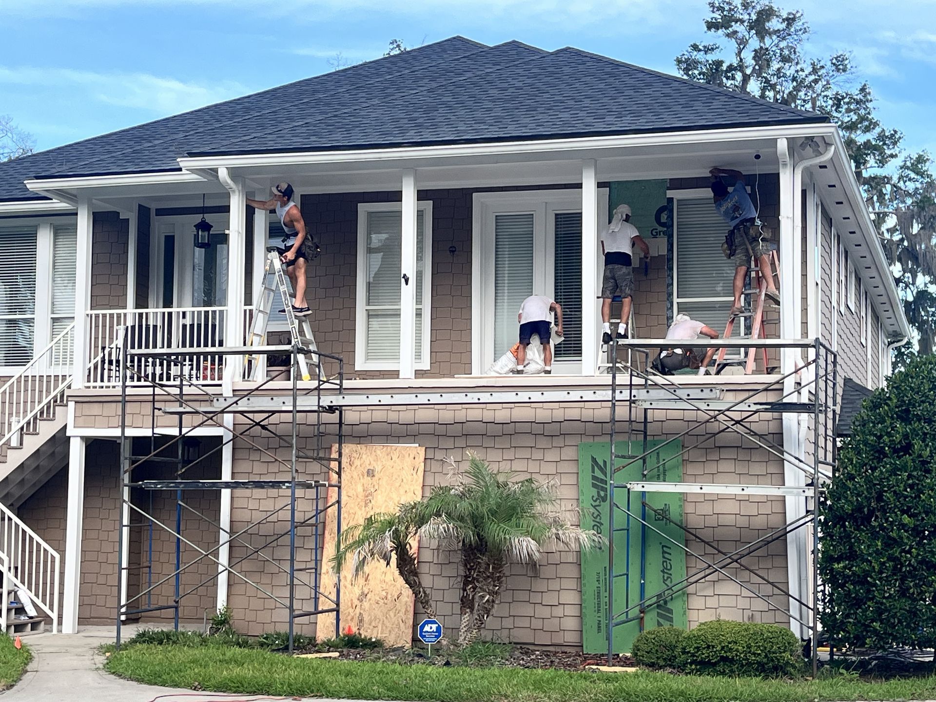 Workers on scaffolding repainting a two-story house with white trim and green lower walls