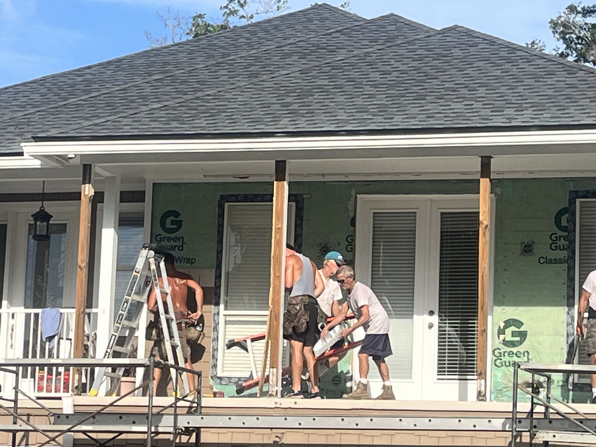Workers repairing a house porch under construction with ladders and tools in front of white shutters