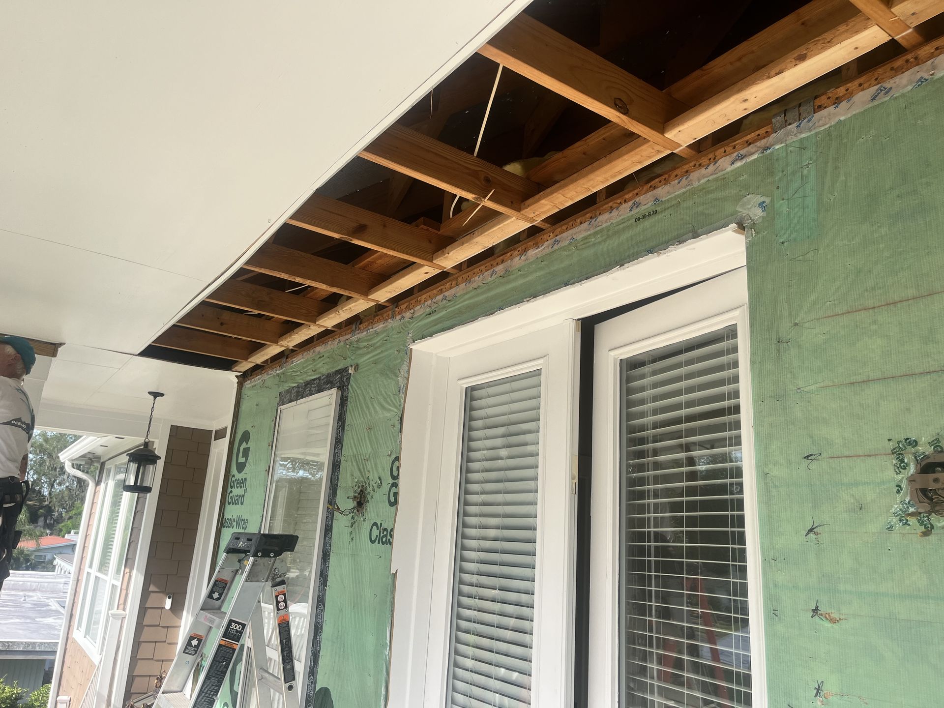 Partially renovated porch with exposed ceiling joists, green wall covering, and white French doors under construction