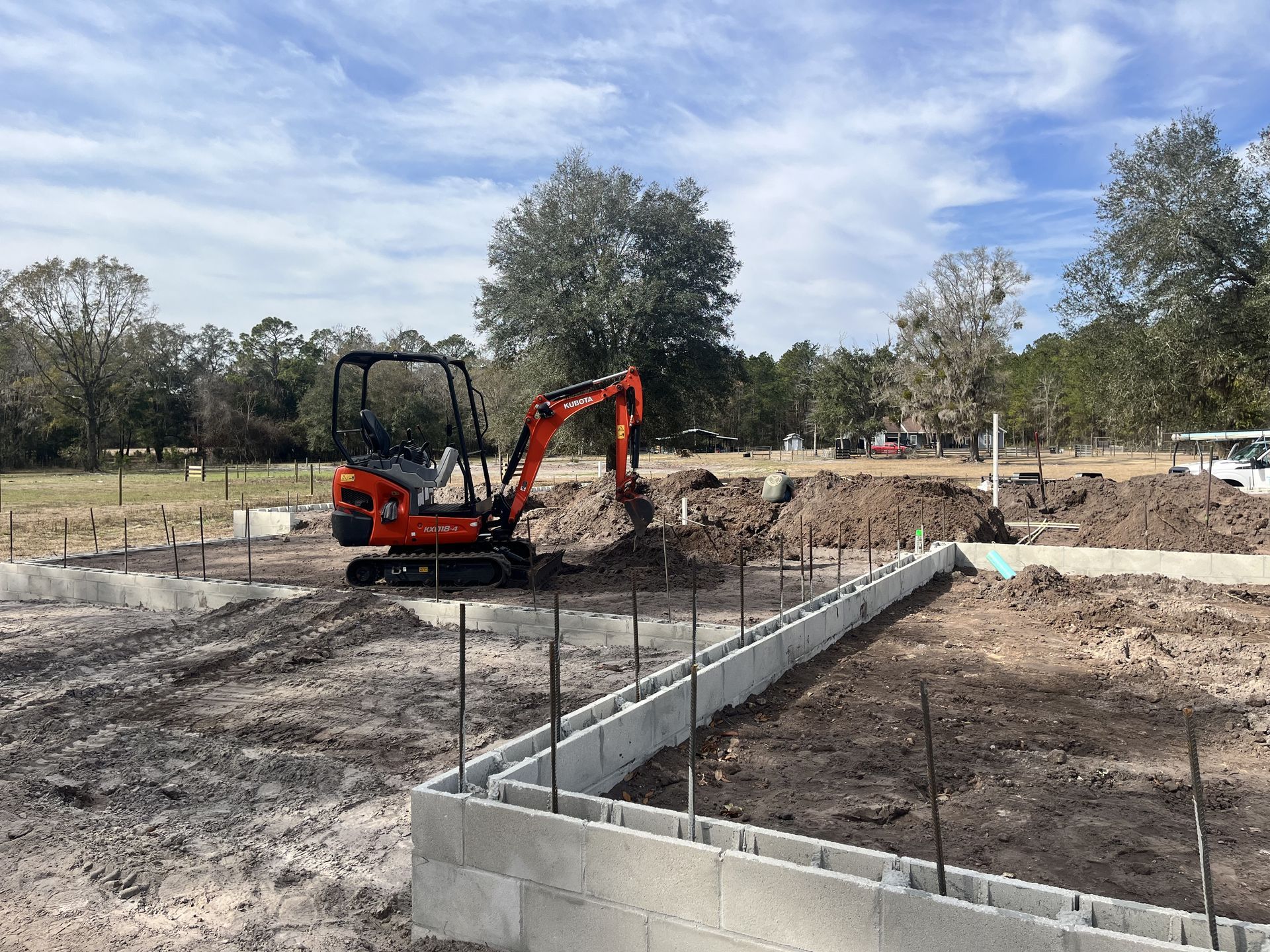 Orange excavator digging on a construction site with concrete foundation walls and rebar in the foreground