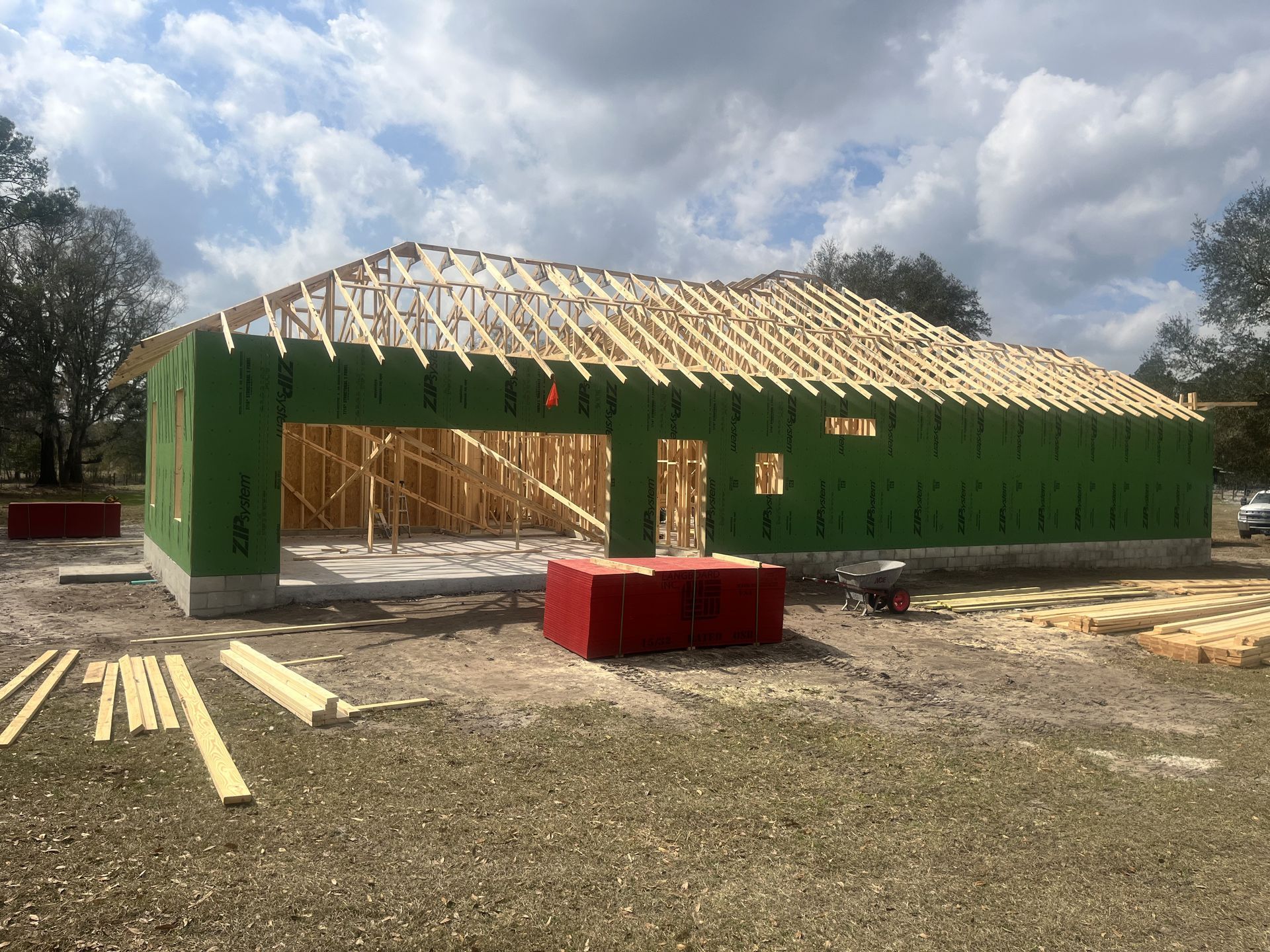 Green house under construction with exposed roof framing and lumber stacked outside.
