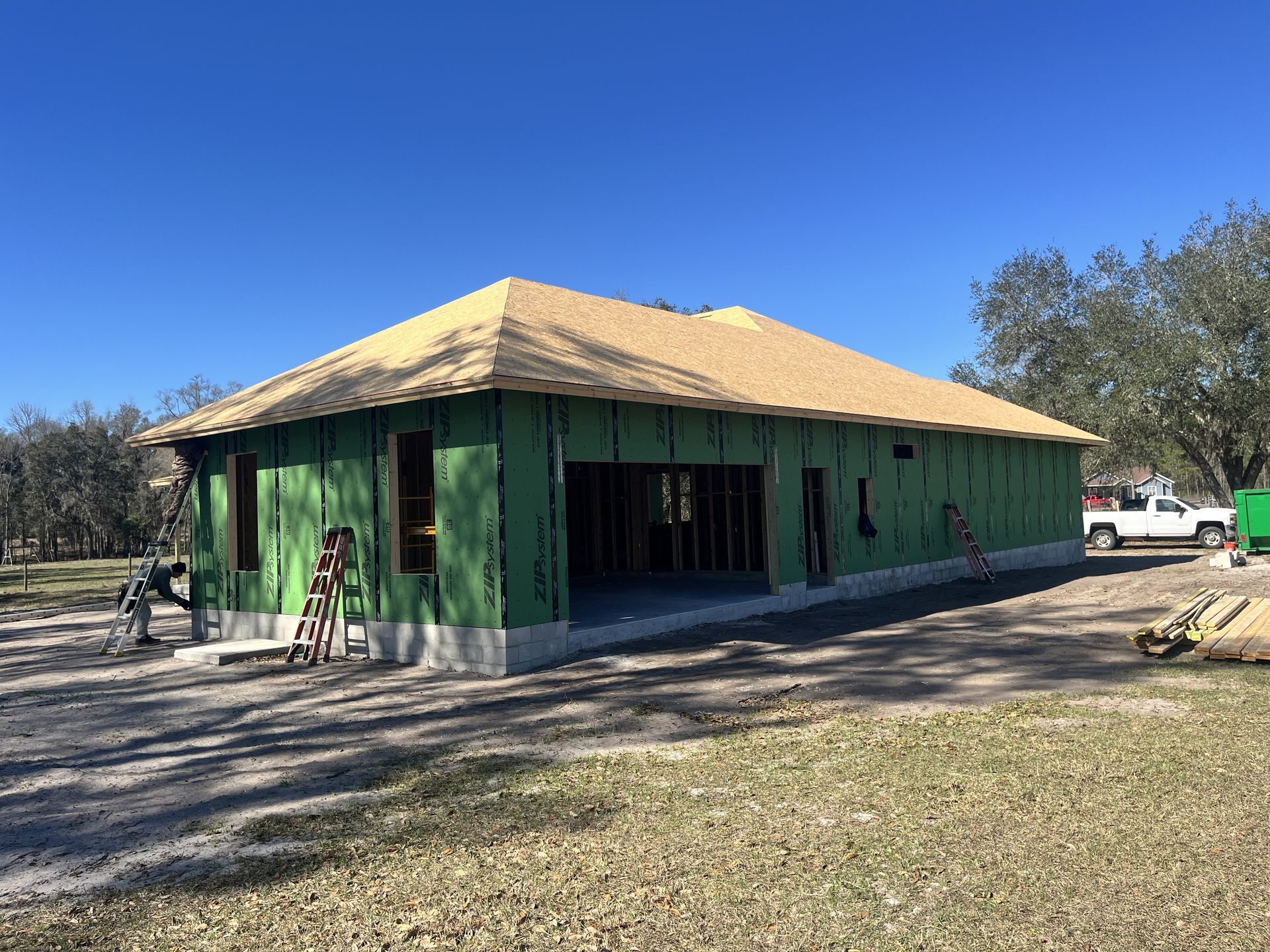 Green house under construction with yellow roof and workers outside on a sunny day