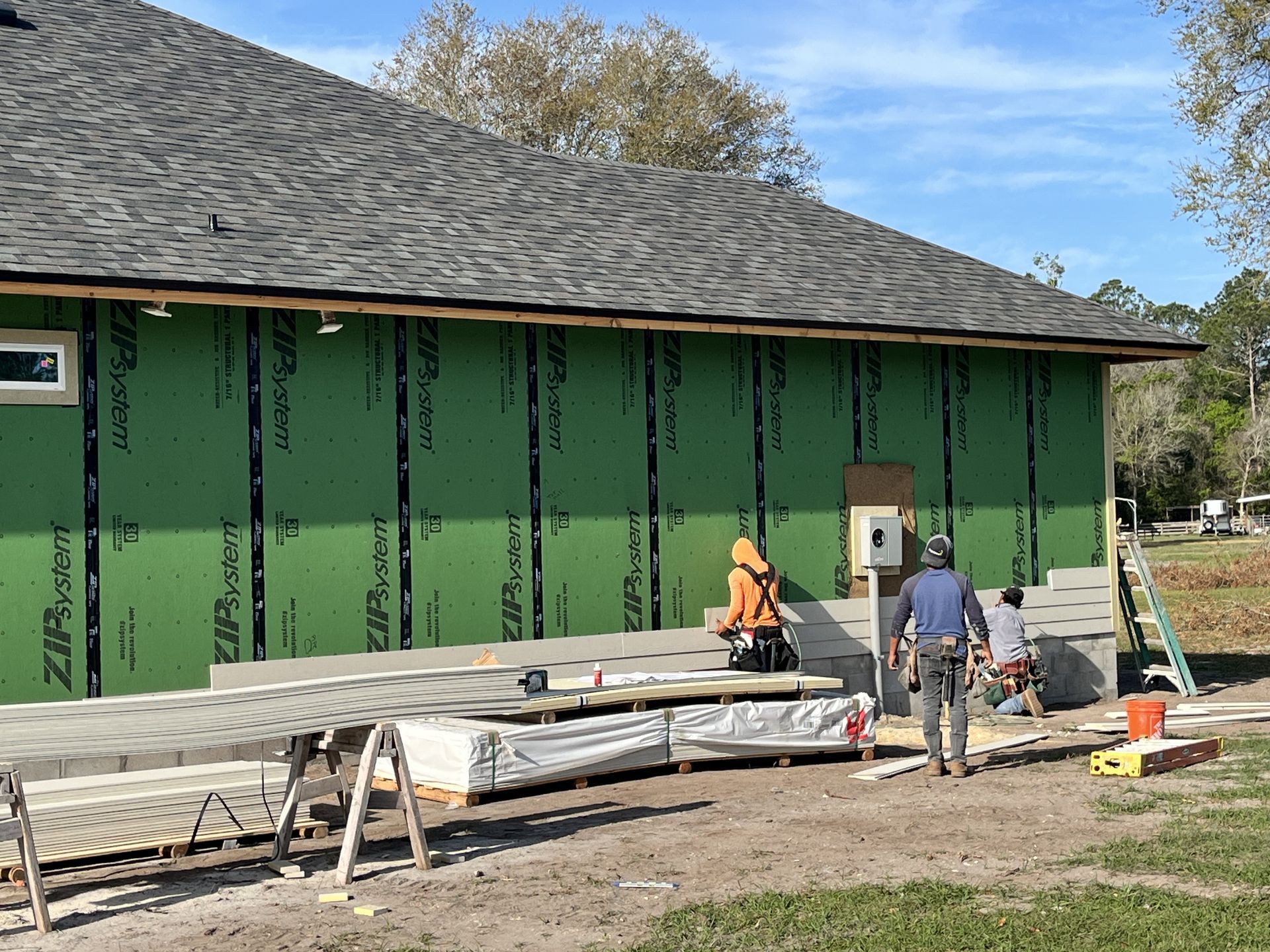 Workers installing siding on a green building under construction near a roof ladder and tools