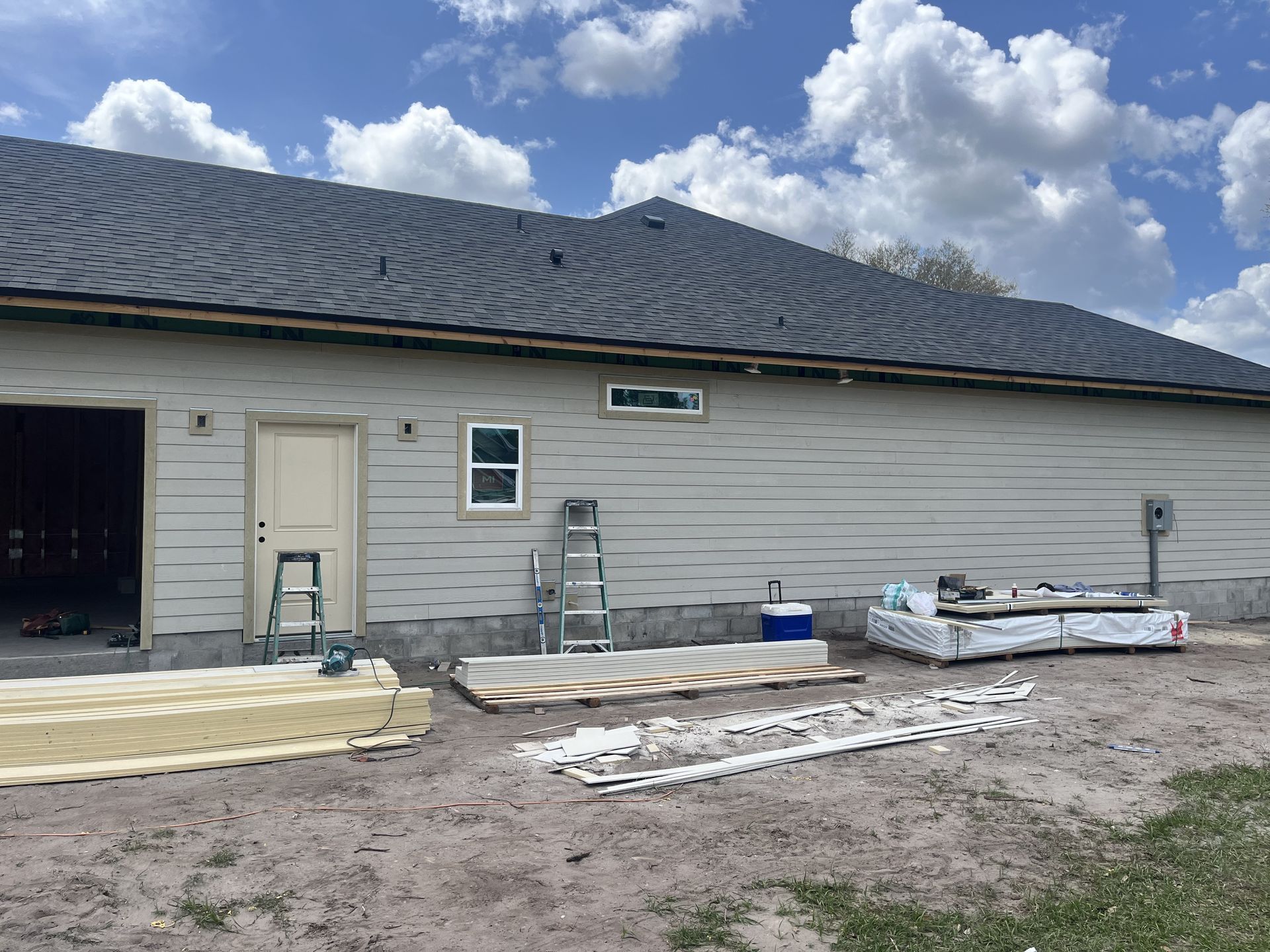 Construction site with a long white building, stacked materials, and a partly cloudy sky.