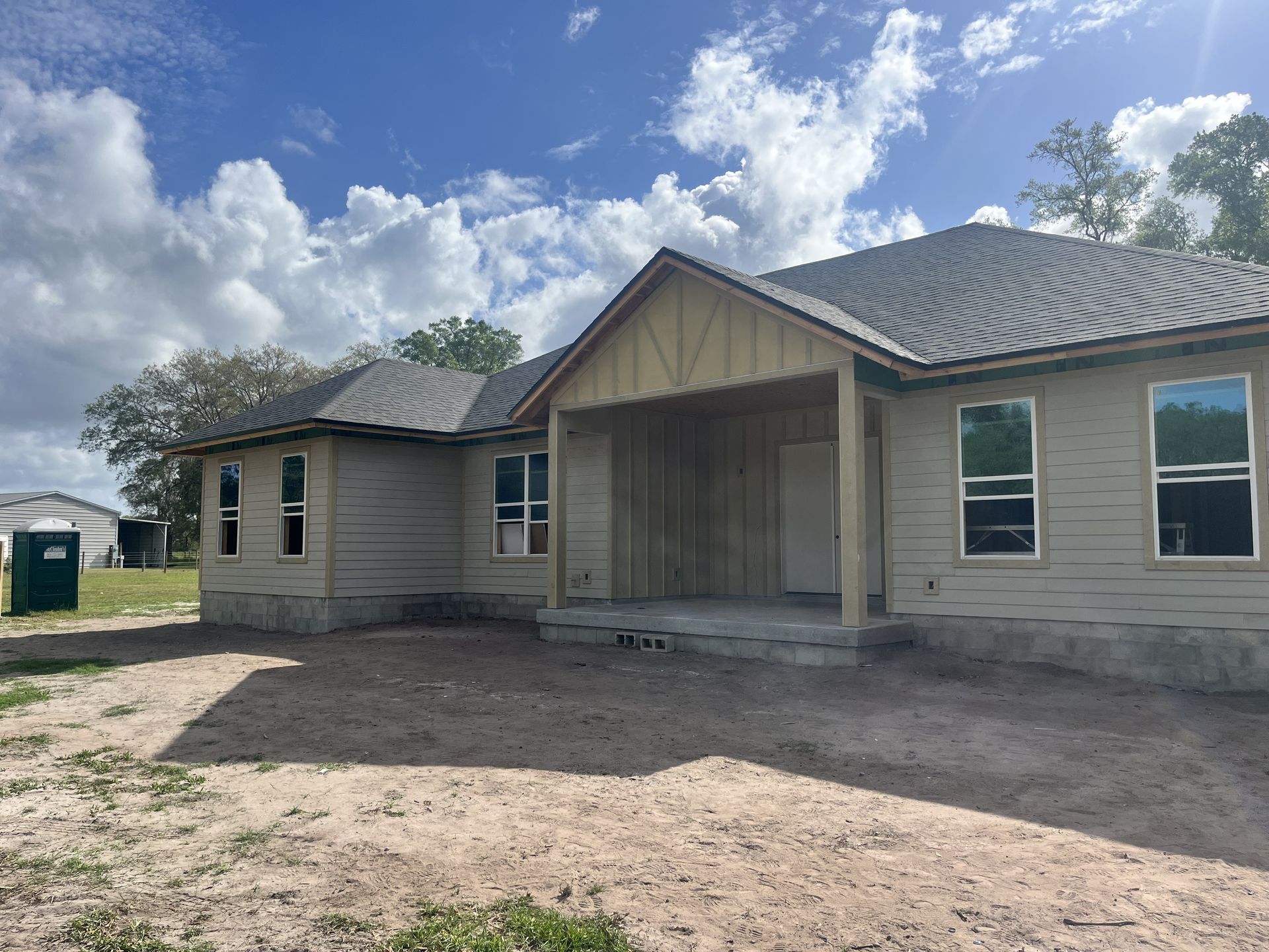 New beige house under construction with covered front porch and dirt yard under cloudy sky